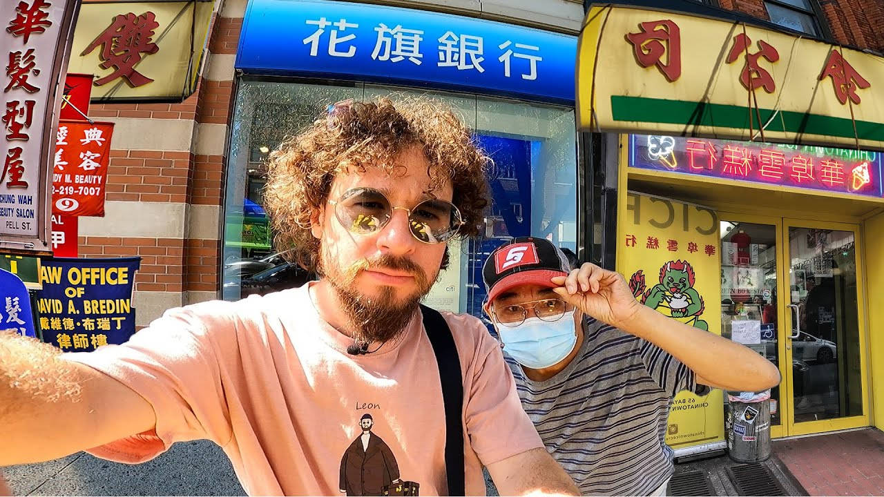Sunglasses 桌布 壁紙 — 兩個男人在色彩繽紛的唐人街商店前自拍，背景有中文招牌和明亮的霓虹燈。