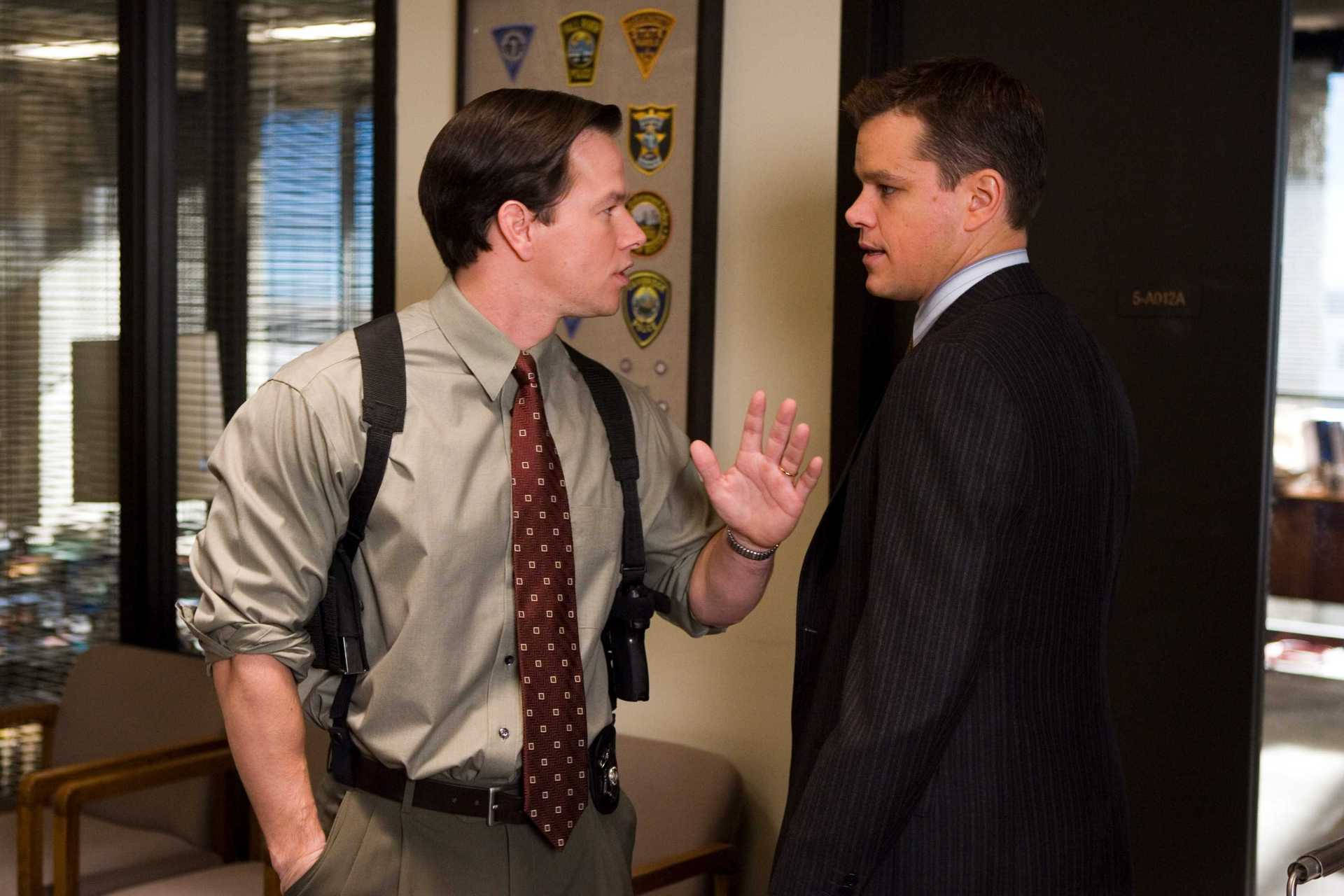 Mark Wahlberg 桌布 壁紙 — 兩個男人在辦公室走廊對峙，一個穿著棕褐色襯衫配吊帶和圖案領帶，另一個穿著深色細條紋西裝。
