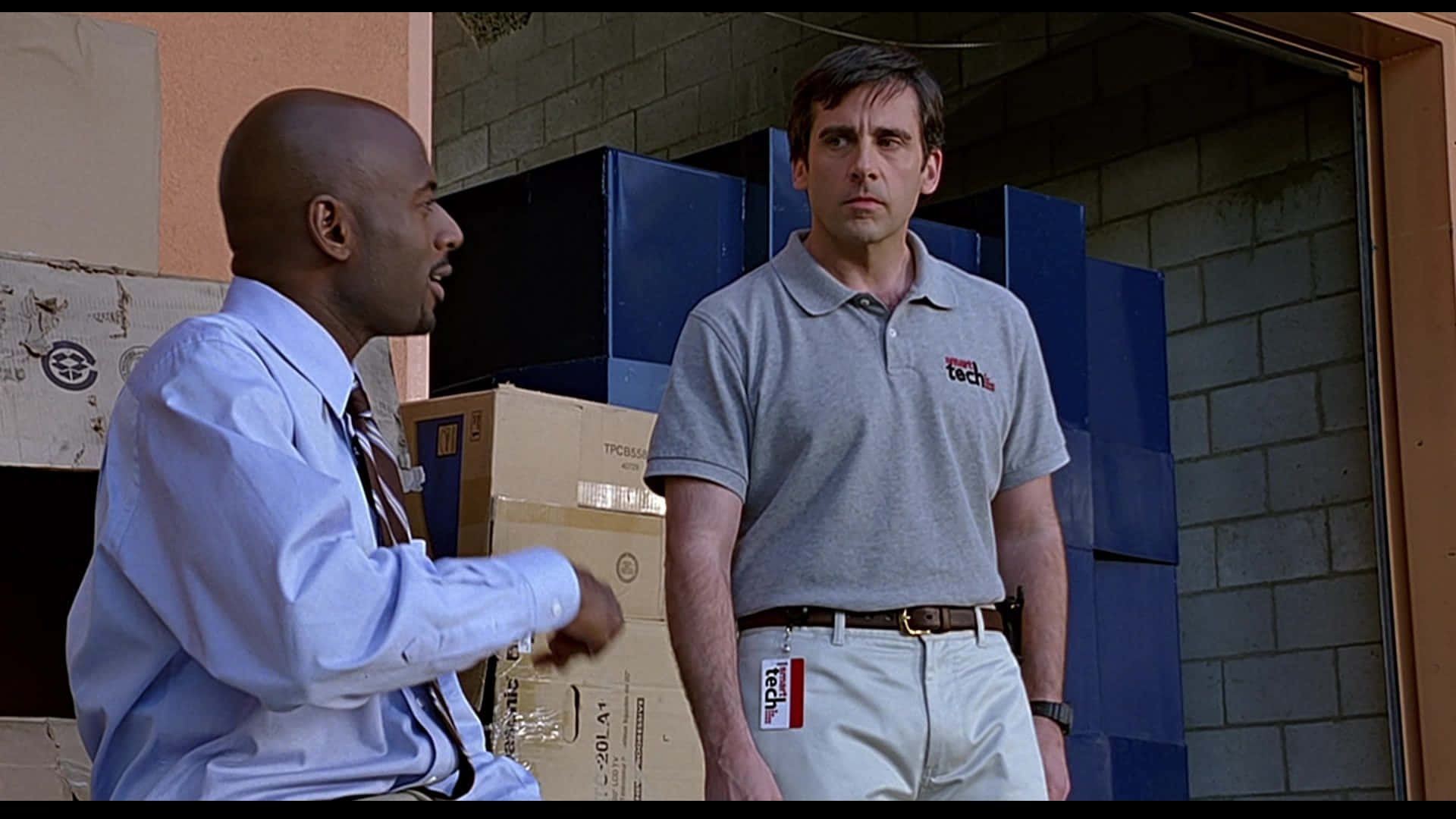 steve carell 桌布 壁紙 — 兩個男人站在倉庫裡，一個邊說話邊做手勢，另一個帶著驚訝的表情凝視著。