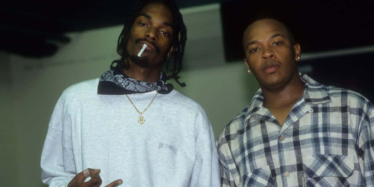 Young Snoop Dogg 桌布 壁紙 — 兩個男人站在室內，一個有辮子頭和香煙，另一個穿著格紋襯衫，兩人都看著相機。