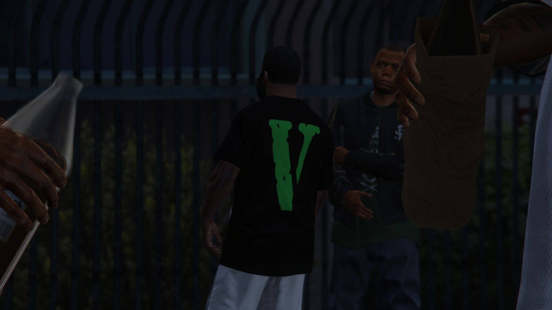 Vlone 桌布 壁紙 — 兩個男人站在昏暗的光線下靠近圍欄，一個穿著帶有綠色V標誌的黑色襯衫，另一個拿著一個棕色袋子。