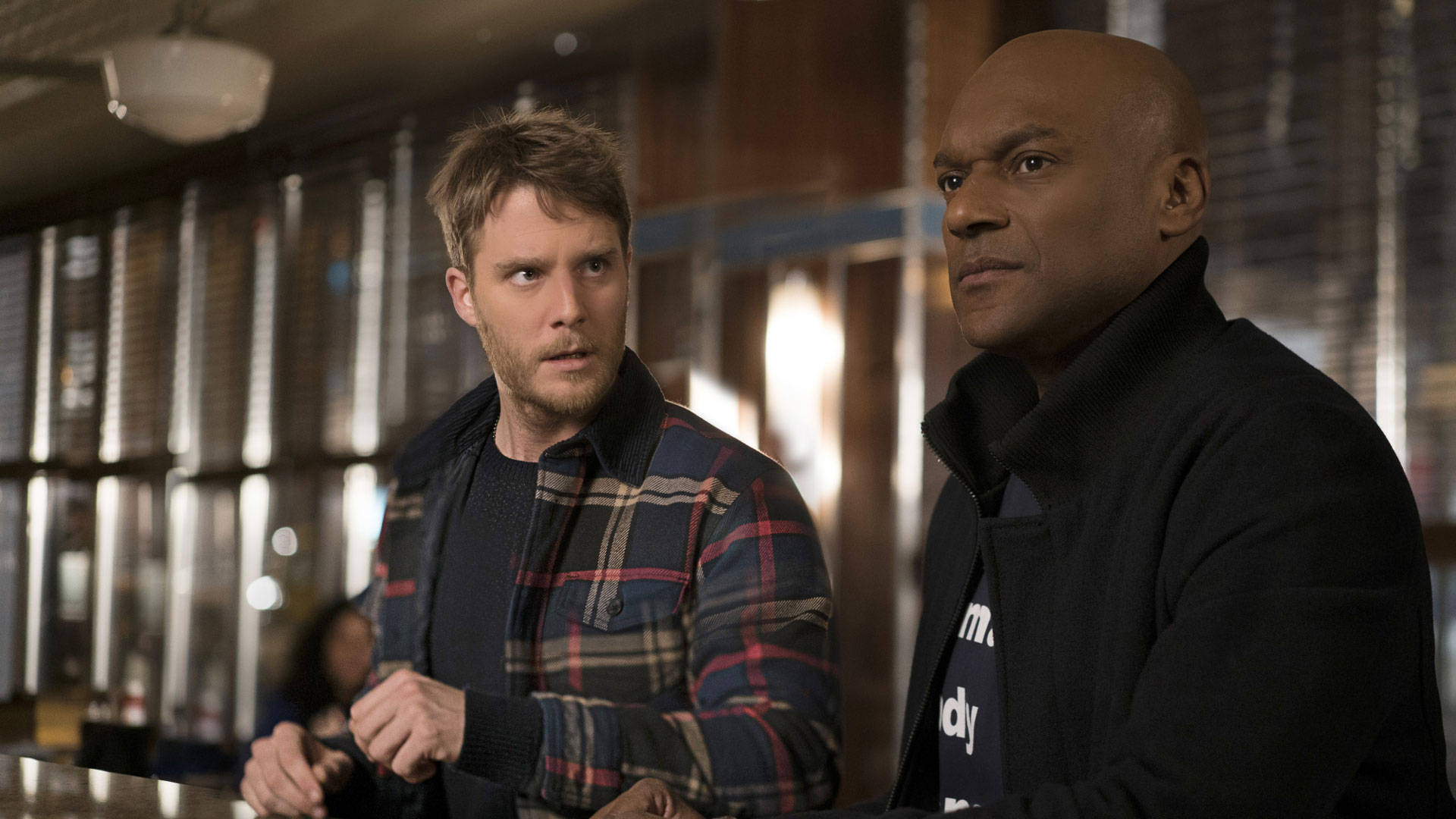 Colin Salmon 桌布 壁紙 — 兩個男人站在燈光昏暗的酒吧裡，神情專注，柔和的光線在他們身後閃爍。
