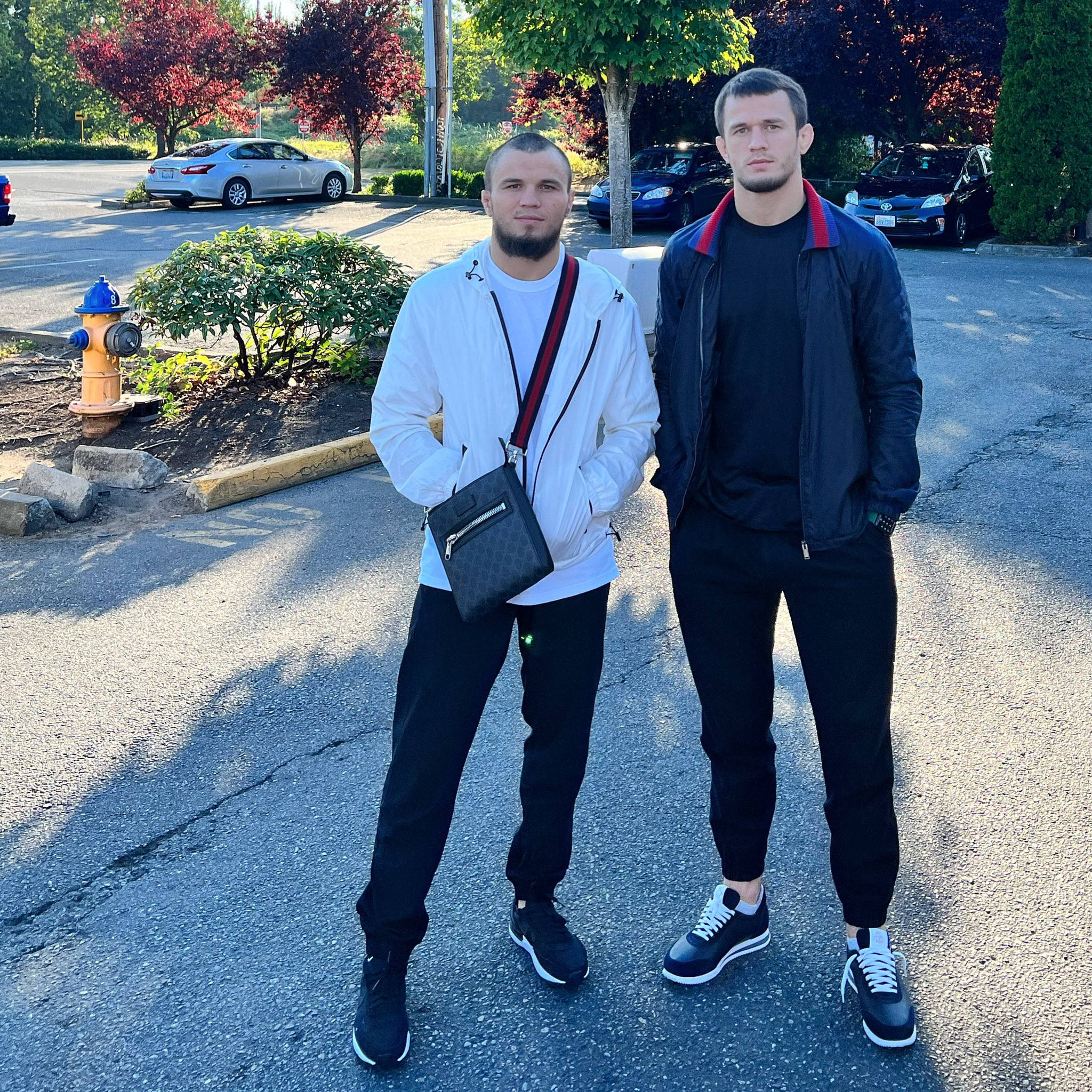 Family 桌布 壁紙 — 兩個男人自信地站在陽光普照的停車場，背景有汽車和樹木。