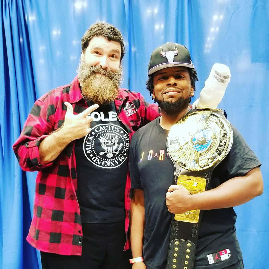 WWE 桌布 壁紙 — 兩個男人開心擺姿勢，其中一人手持冠軍腰帶，背景為藍色窗簾。