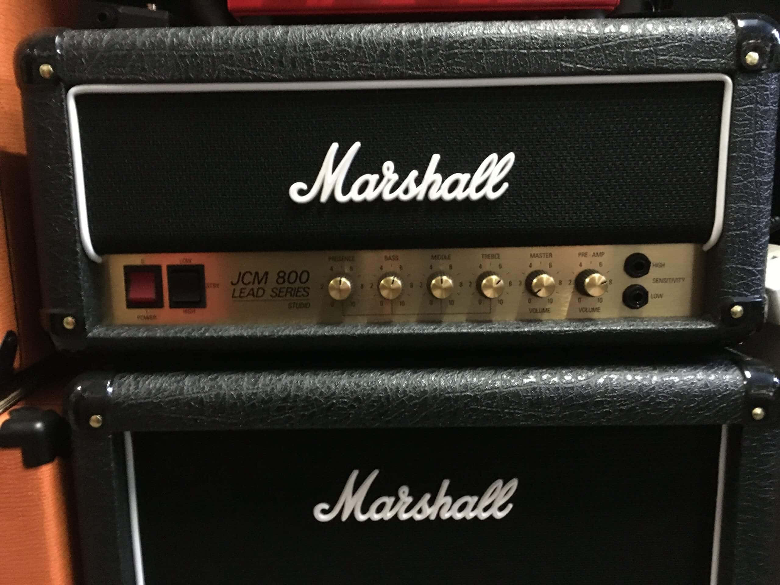 Marshall 桌布 壁紙 — 兩個疊放的黑色 Marshall JCM 800 吉他擴大機，帶有金色旋鈕和白色手寫標誌，背景為溫暖的木質。