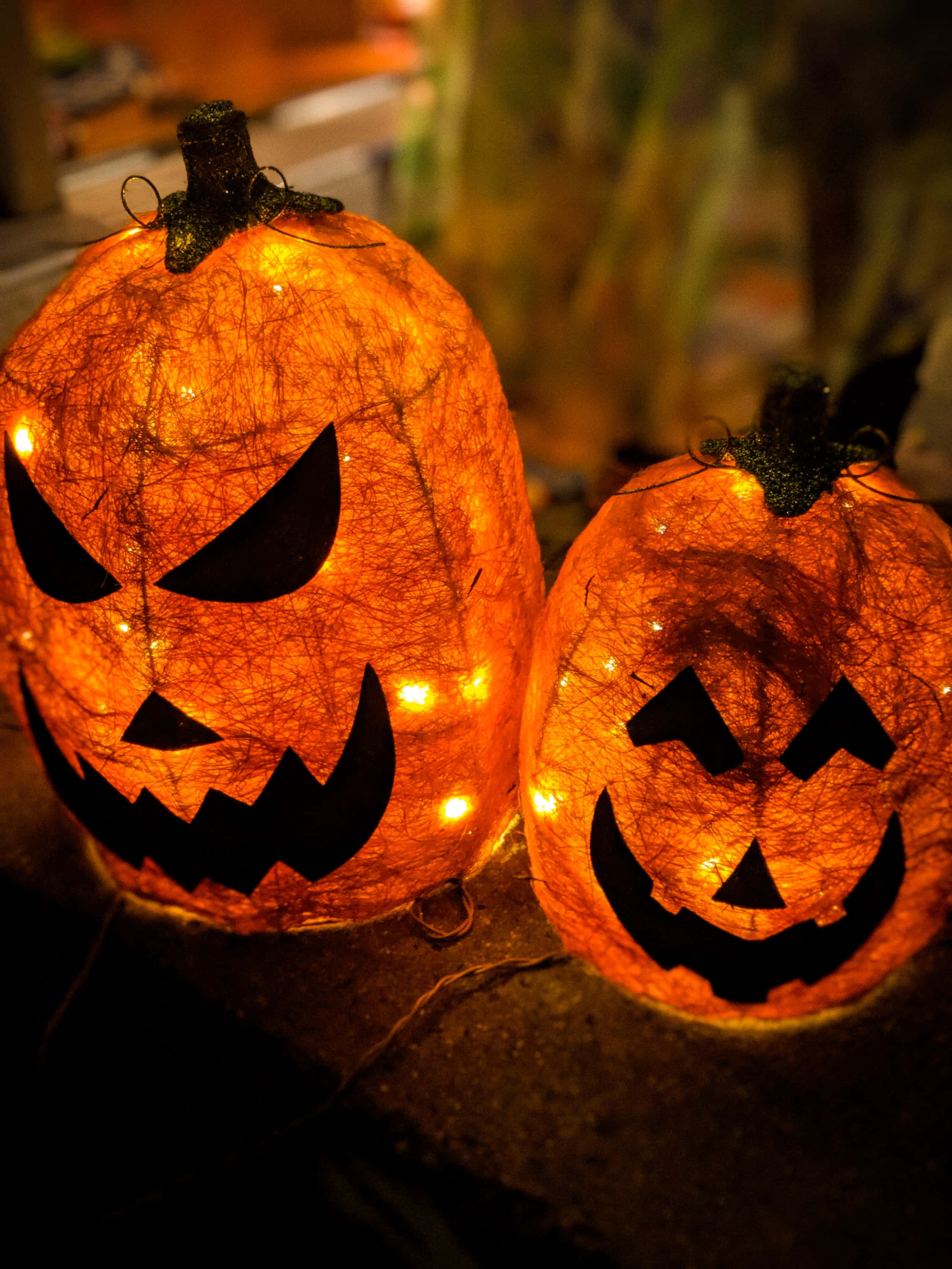 jack o'lantern 桌布 壁紙 — 兩個發光的傑克南瓜燈，帶有絲狀橙色外皮和兇惡的面孔，在黑暗的戶外環境中投射出溫暖的光芒。