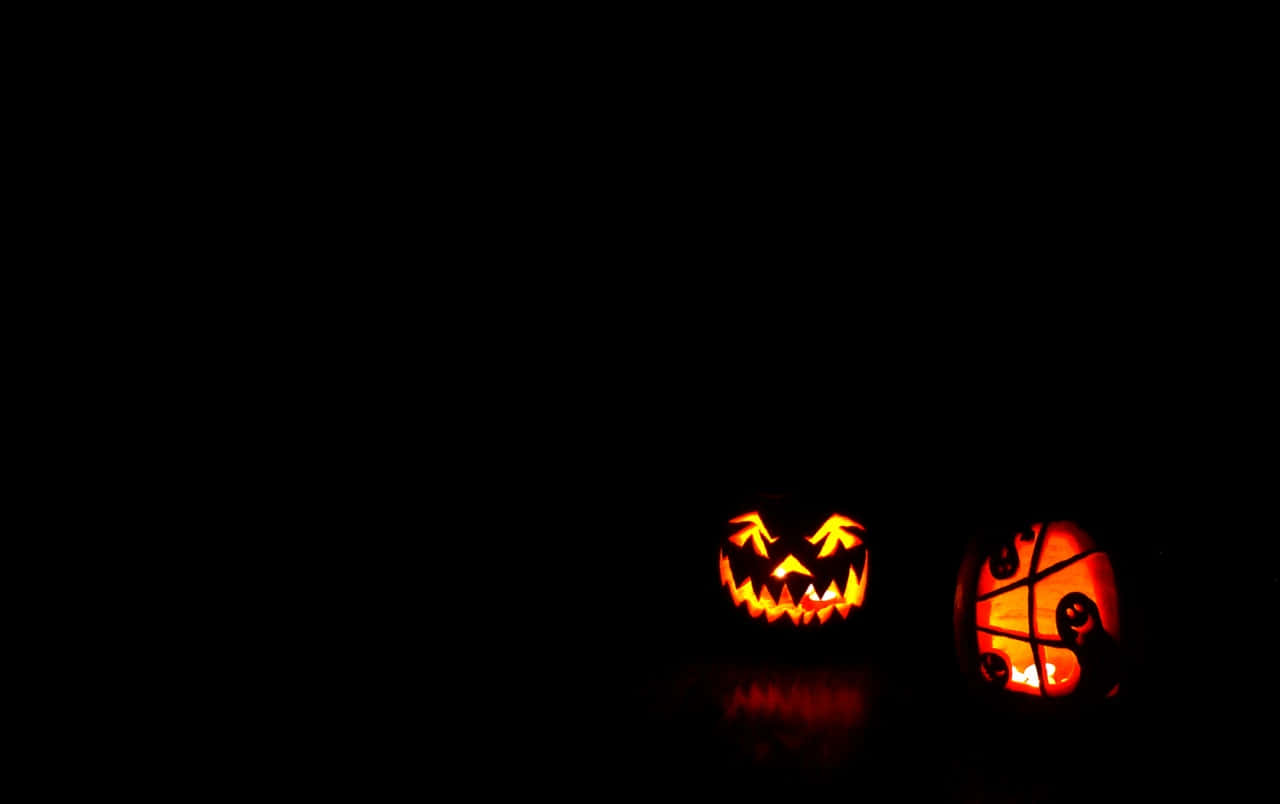Pumpkin Carving 桌布 壁紙 — 兩個發光的傑克南瓜燈，帶有雕刻面孔和籃球設計，用溫暖的橙色光芒照亮黑暗場景。