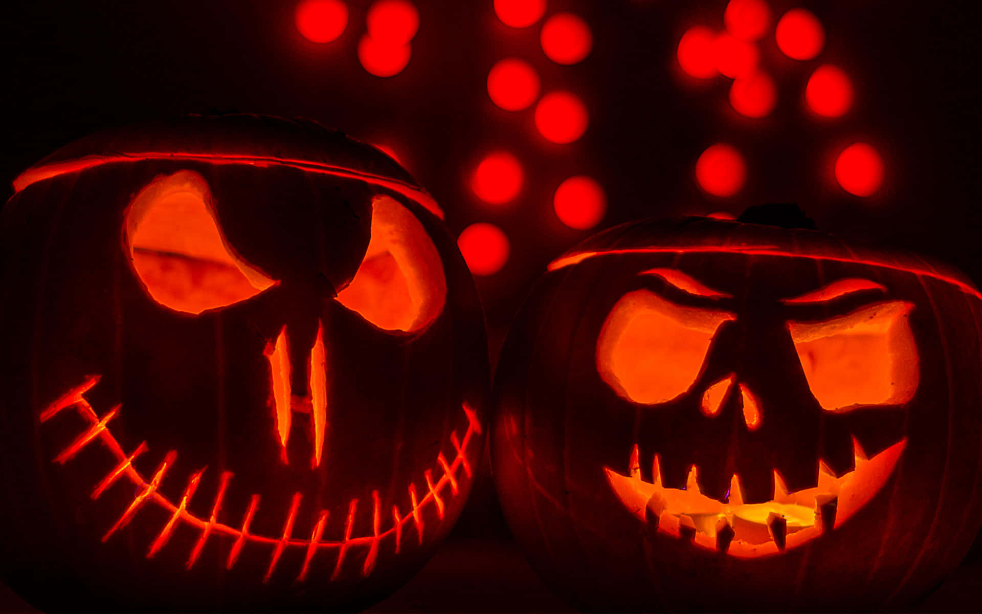Pumpkin 桌布 壁紙 — 兩個發光的南瓜燈，帶有威脅性的雕刻面孔，從內部照亮，背景為深色，帶有紅色散景燈光。