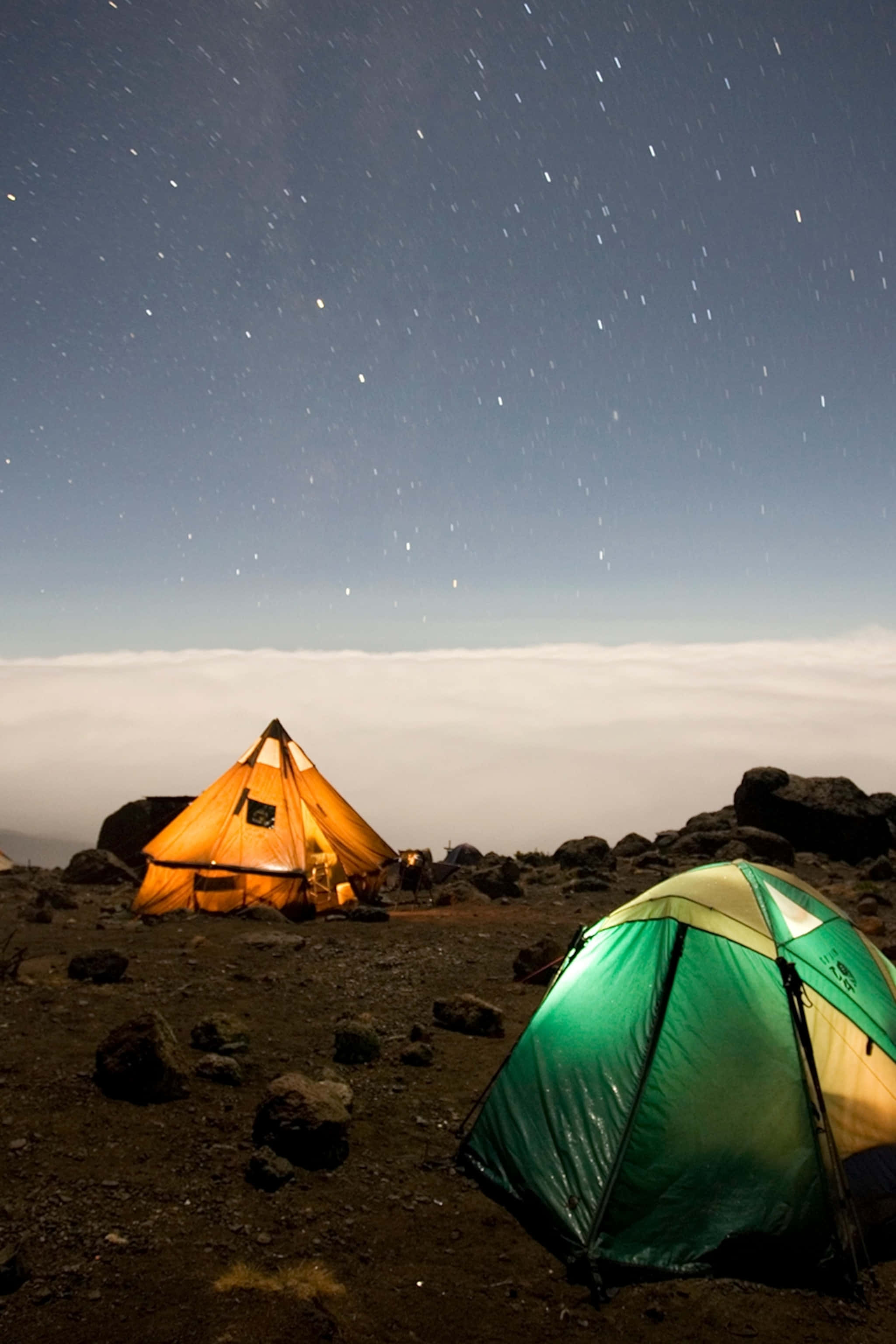 Camping 桌布 壁紙 — 兩個發光的帳篷在岩石山頂上，在星空的雲海下露營。