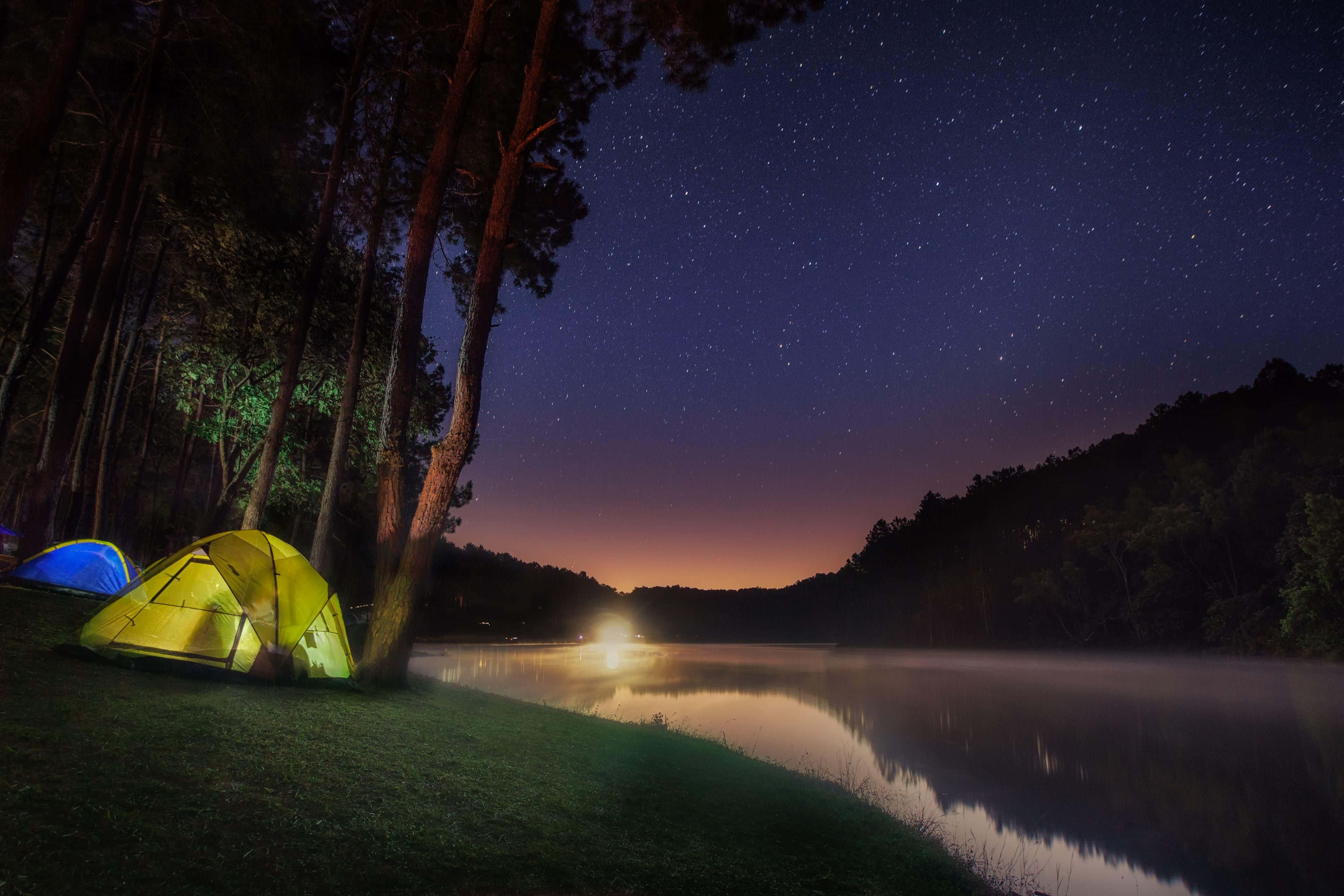 Lake 桌布 壁紙 — 兩個發光的帳篷坐落在星空下，旁邊是一個霧氣瀰漫的湖泊，倒映著遠處的燈光。