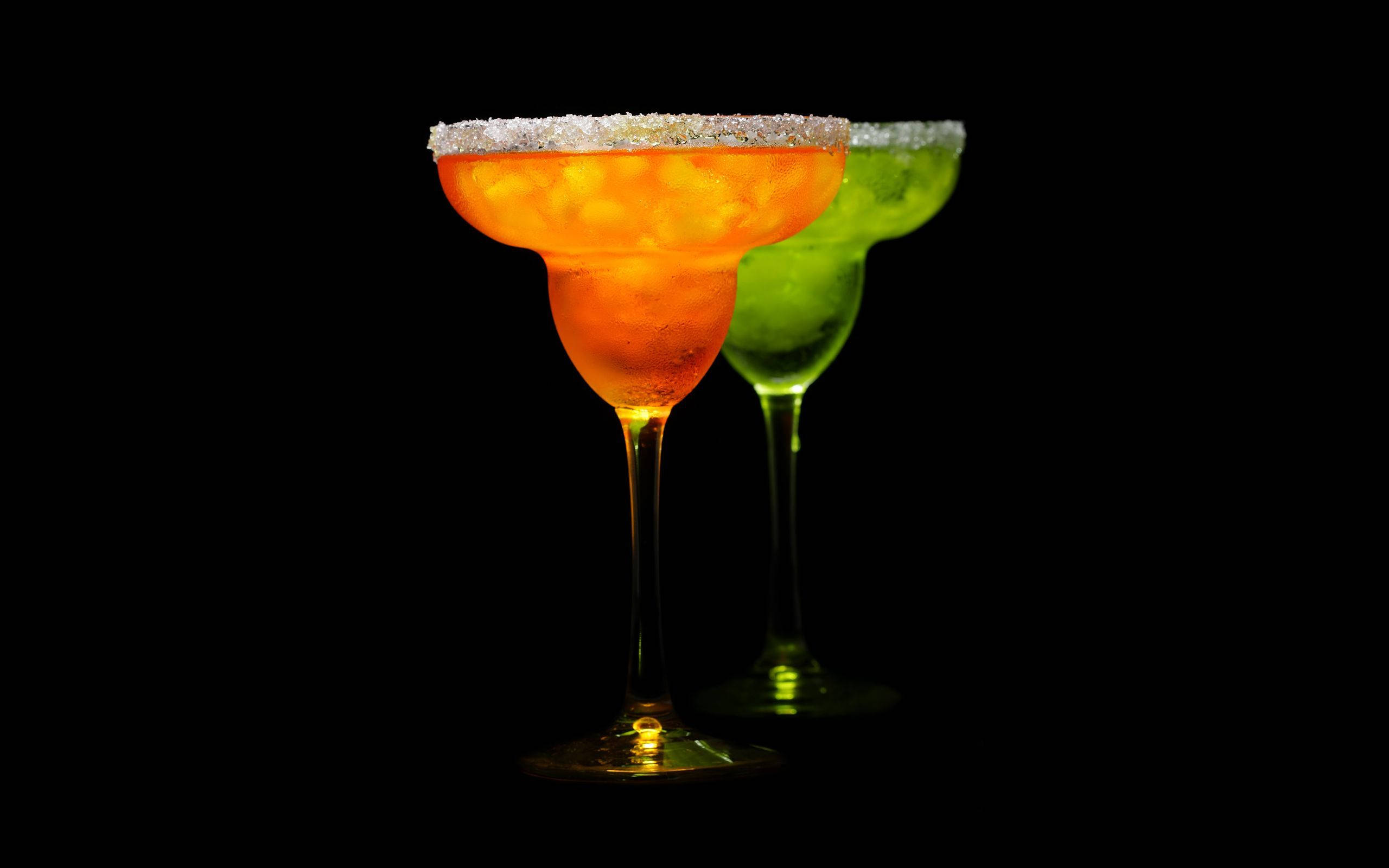alcohol 桌布 壁紙 — 兩個發光的瑪格麗特杯，杯口沾有糖邊，一個橙色一個綠色，立在純黑色背景前。