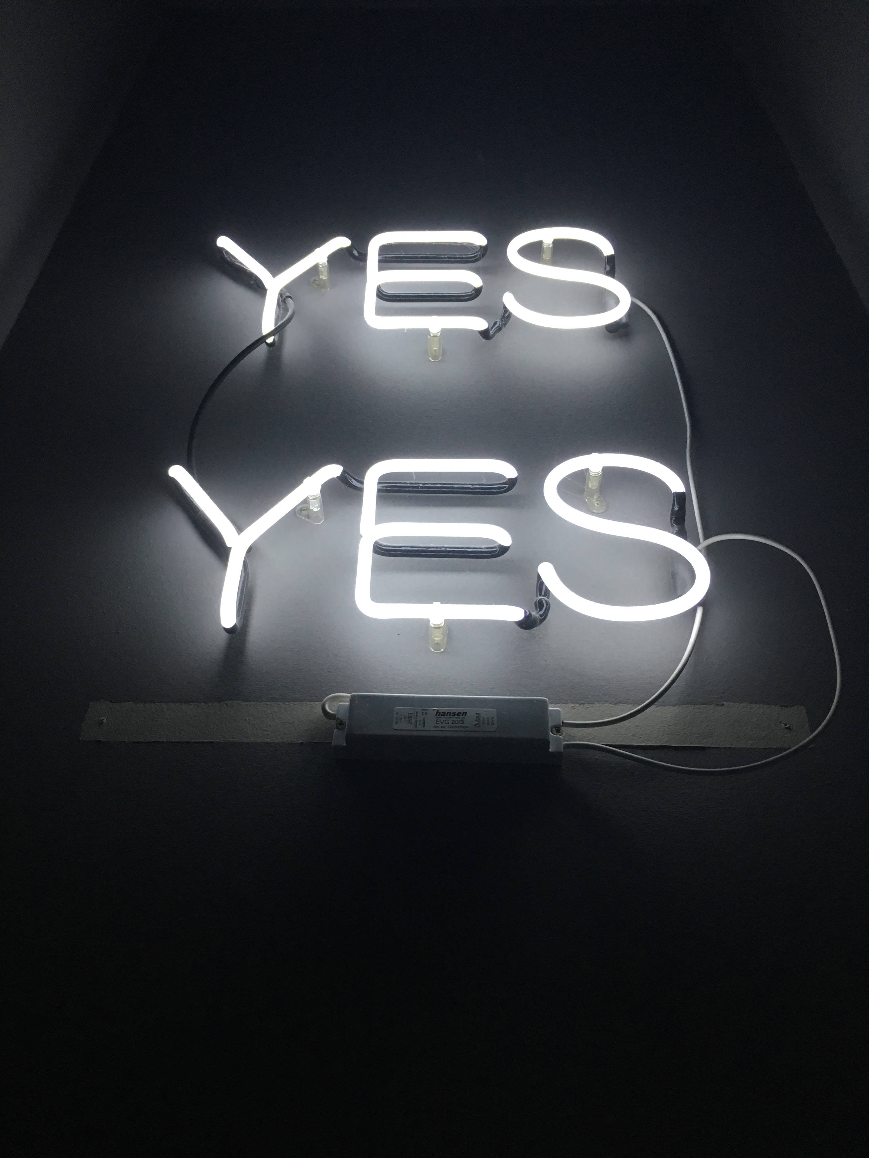 lights 桌布 壁紙 — 兩個發光的白色霓虹燈牌，垂直堆疊在深色牆壁上，拼出YES，極簡風格。
