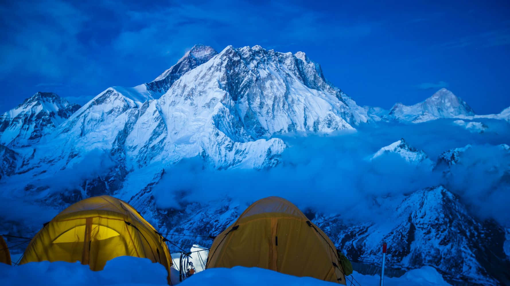 Mount Everest 桌布 壁紙 — 兩個發光的黃色帳篷依偎在雪地中，位於高聳的藍色調雪山腳下，天空暮色蒼茫。