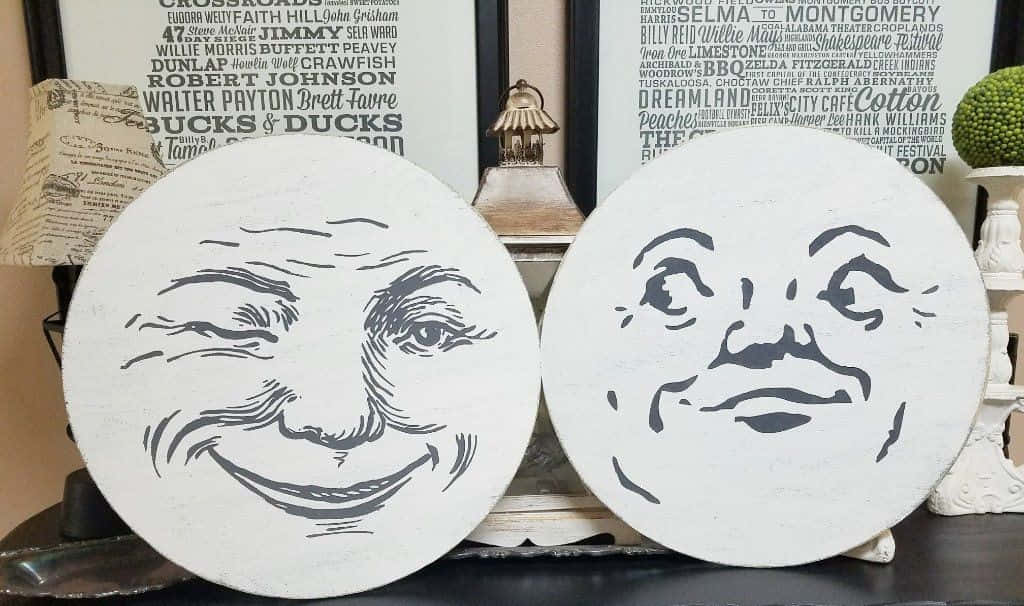 Moon Face 桌布 壁紙 — 兩個白色圓形牌匾，帶有黑色線條藝術，描繪微笑的月亮臉，放在一個深色架子上，旁邊是復古裝飾。