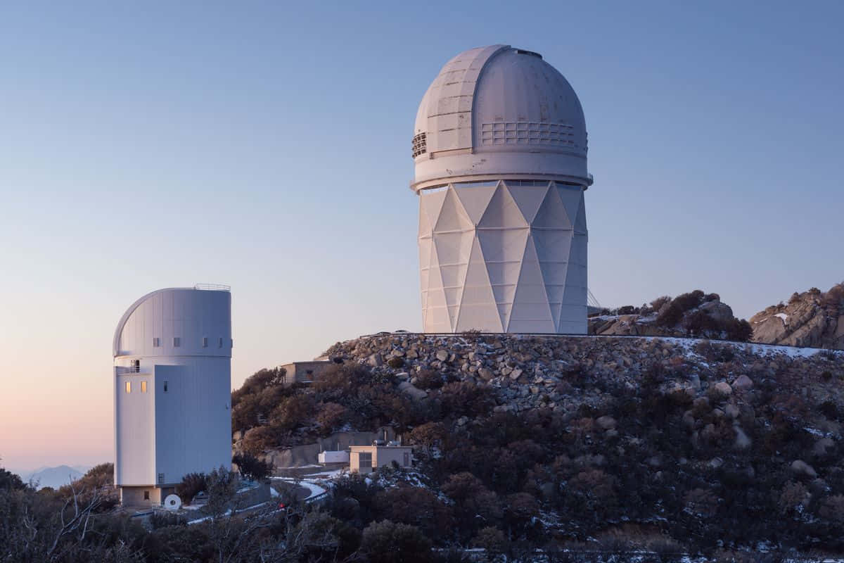 Observatory 桌布 壁紙 — 兩個白色天文台圓頂棲息在岩石山坡上，覆蓋著薄雪，在清澈的暮色天空下。