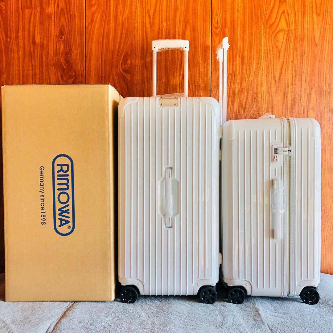 手機 桌布 壁紙 — 兩個白色條紋Rimowa行李箱站在其品牌紙箱旁邊，背景是溫暖的木牆。