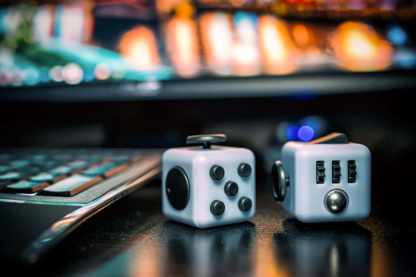 Fidget 桌布 壁紙 — 兩個白色減壓方塊放在一張深色桌子上，旁邊有一個鍵盤，背景中有一個發光的顯示器。