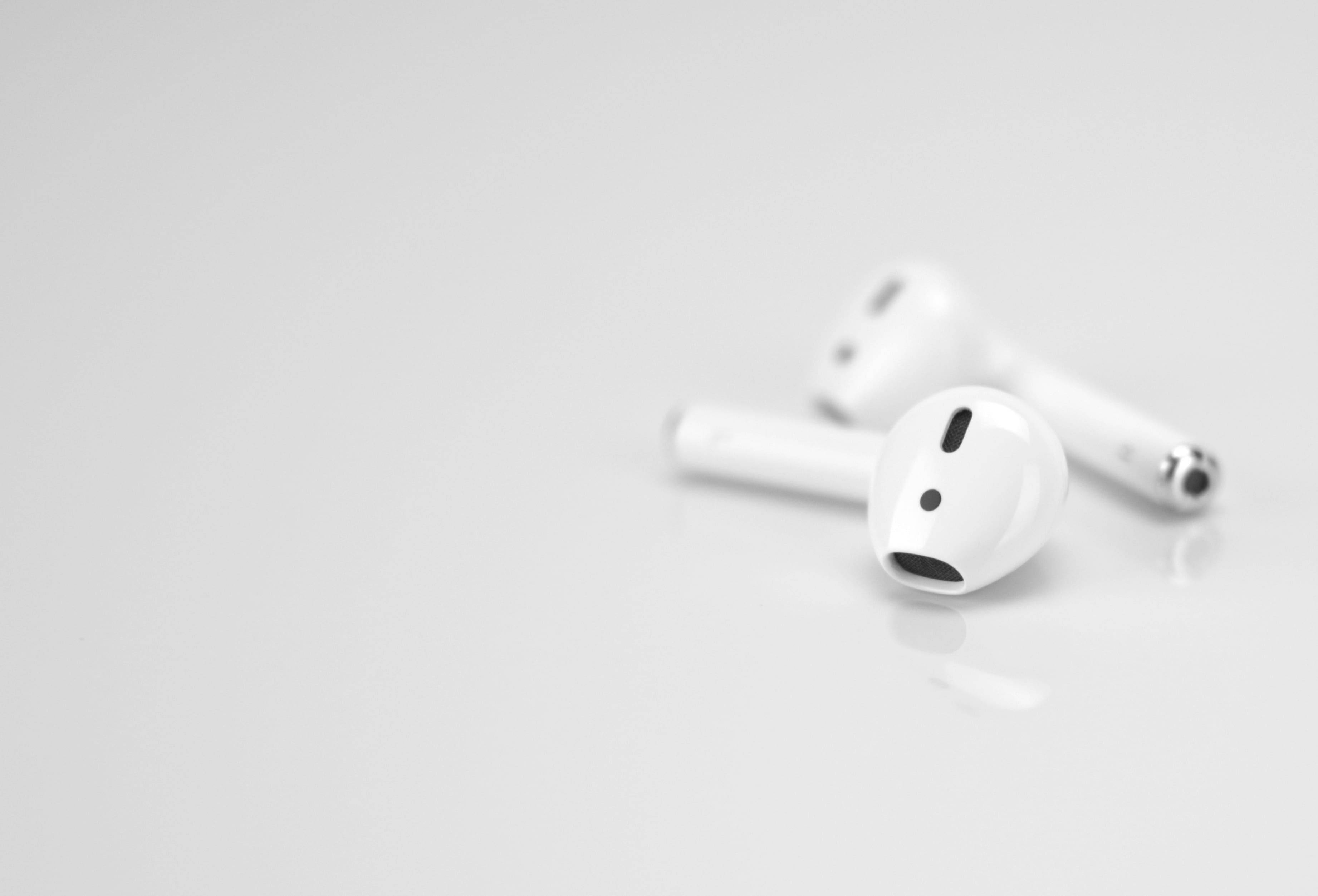 AirPods 桌布 壁紙 — 兩個白色無線耳塞放置在一個極簡風格的反射表面上，帶有柔和陰影和淺景深。