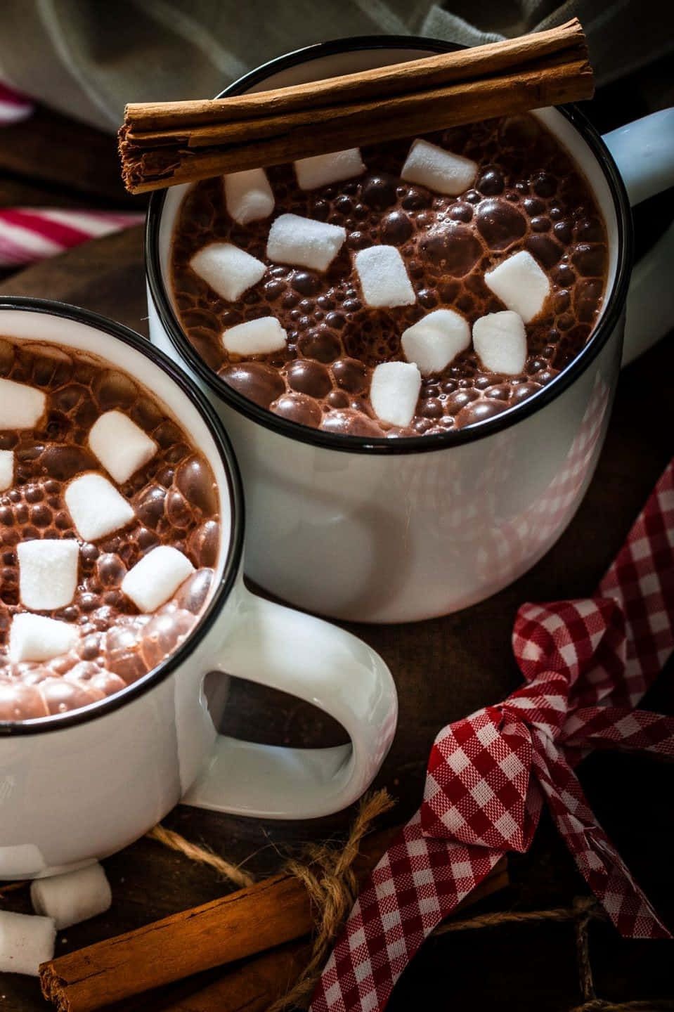 Hot Chocolate 桌布 壁紙 — 兩個白色琺瑯杯，裝滿冒著熱氣的熱巧克力，上面放有棉花糖和肉桂棒，置於鄉村風木桌上。