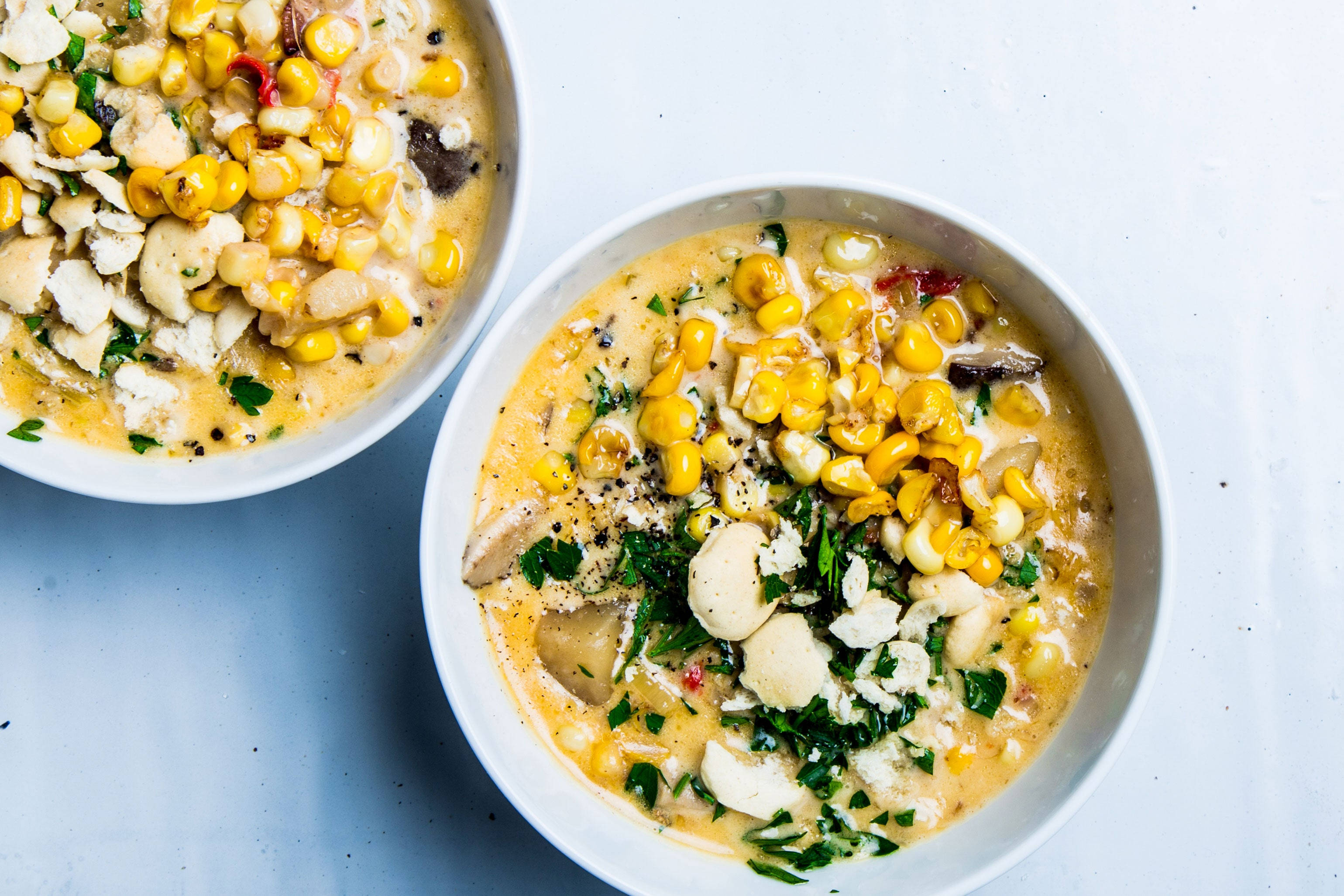 Chowder 桌布 壁紙 — 兩個白色碗裝滿了奶油玉米和白豆湯，上面撒上新鮮香草和黑胡椒。