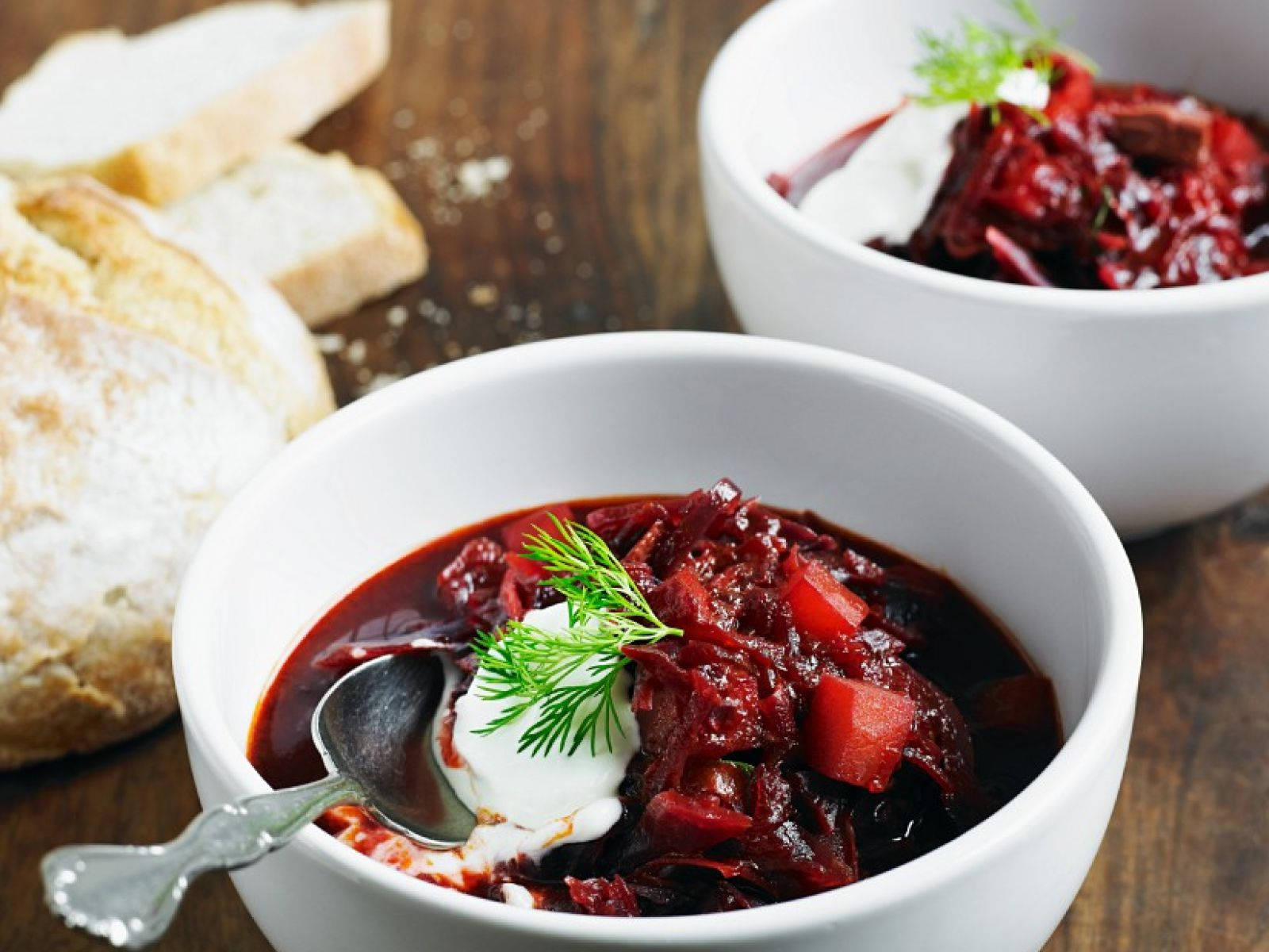 beetroot 桌布 壁紙 — 兩個白色碗裝滿濃郁的紅羅宋湯，上面放有酸奶油和新鮮蒔蘿，旁邊有脆皮麵包，放在質樸的木桌上。