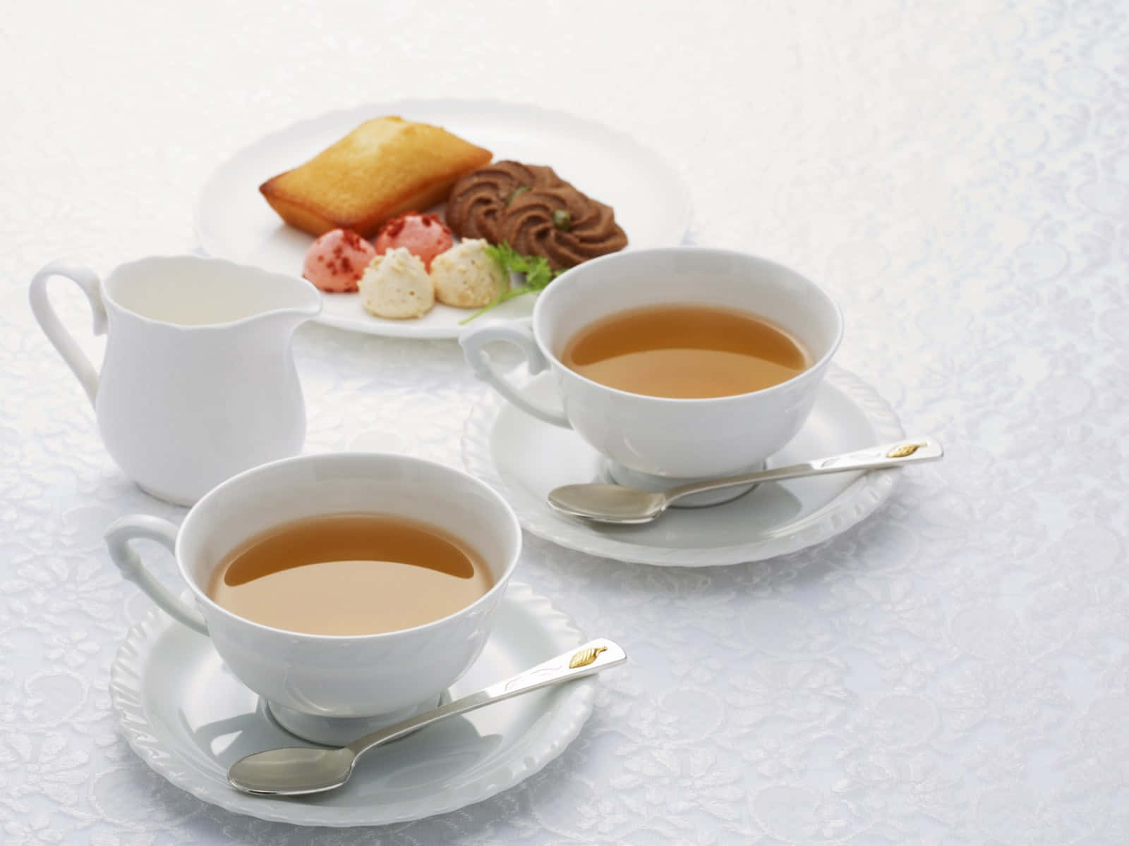 咖啡動圖 桌布 壁紙 — 兩個白色茶杯，內有茶和湯匙，放在一個蕾絲桌布上，旁邊有一碟糕點。
