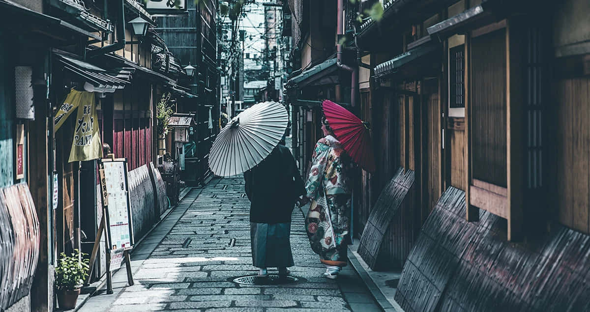 Elusive 桌布 壁紙 — 兩個穿著傳統日本服飾的人物，撐著紙傘，沿著一條狹窄的木巷走著。