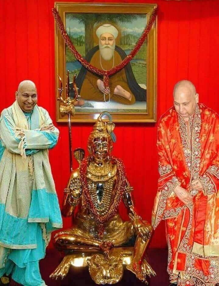 guru nanak dev ji 桌布 壁紙 — 兩個穿著傳統長袍的男人站在金色神像旁邊，上方掛著一個帶框的肖像，背景是紅色窗簾。