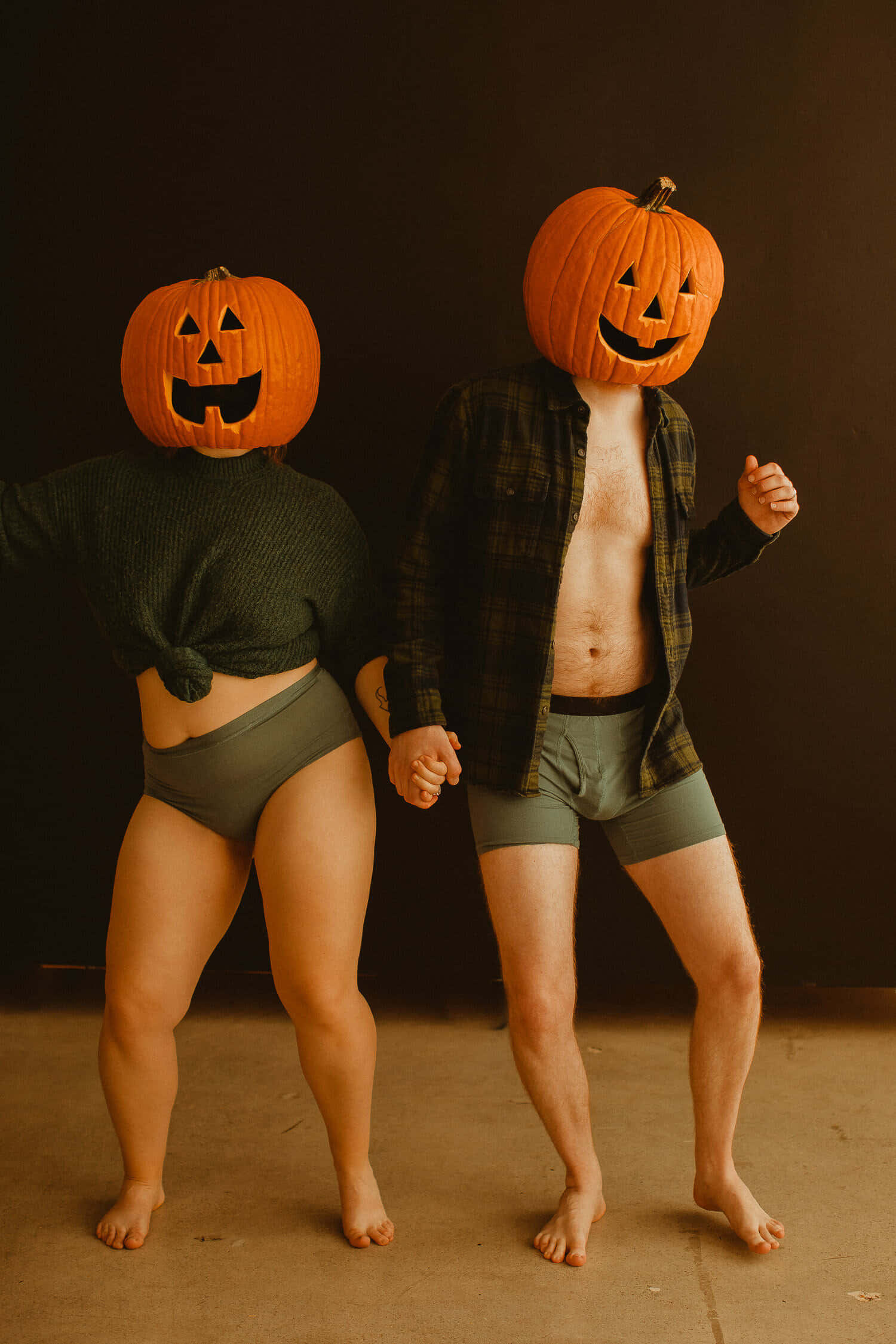 Halloween Pumpkin 桌布 壁紙 — 兩個穿著內衣的人戴著雕刻南瓜頭，在黑暗的攝影棚背景下牽手。