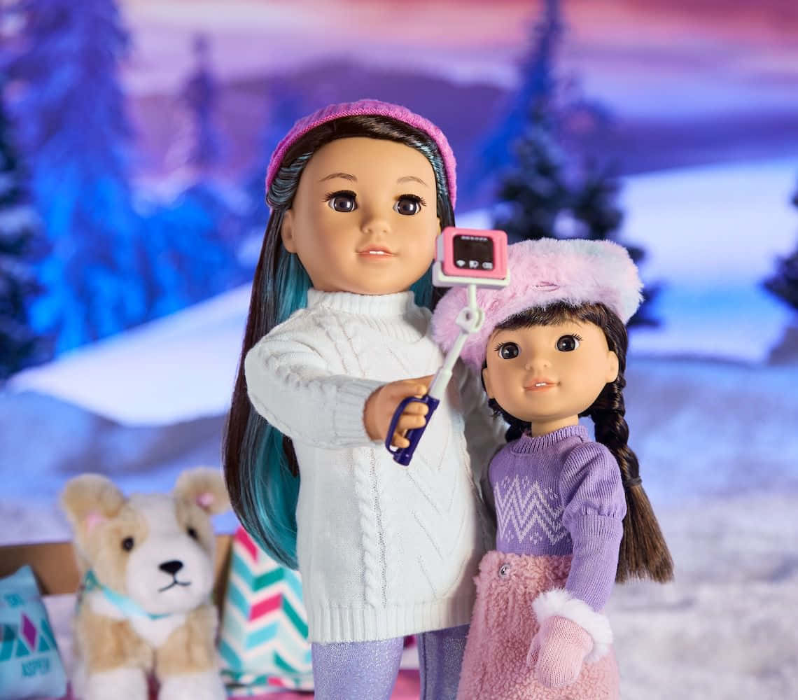 american girl 桌布 壁紙 — 兩個穿著冬季裝備的玩偶在黃昏時分，以雪地森林為背景，用自拍棒擺姿勢。