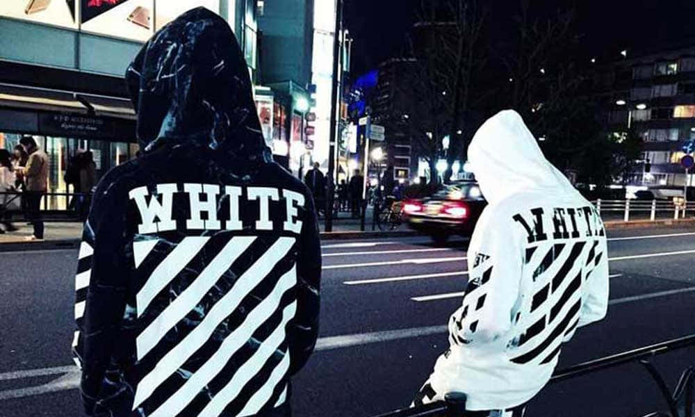 Off White 桌布 壁紙 — 兩個穿著印有「WHITE」字樣的黑白連帽衫的人，在夜晚霓虹燈照亮的城市街道上背對背站立。