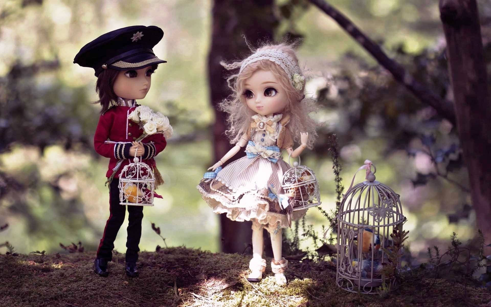cute doll couple 桌布 壁紙 — 兩個穿著復古服裝的精緻洋娃娃站在陽光明媚的森林中，每人手持一個鳥籠，裡面有一隻鳥。