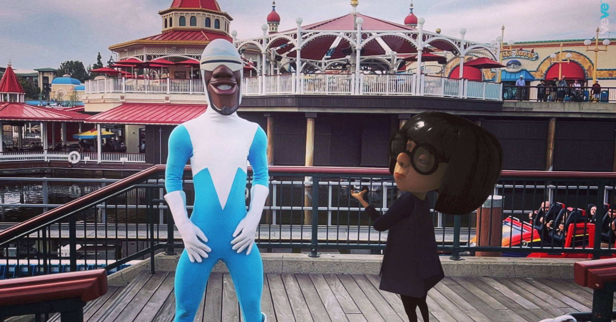 Frozone 桌布 壁紙 — 兩個穿著戲服的動畫角色在主題公園的木製碼頭上擺姿勢，背景是色彩繽紛的建築物和遊樂設施。