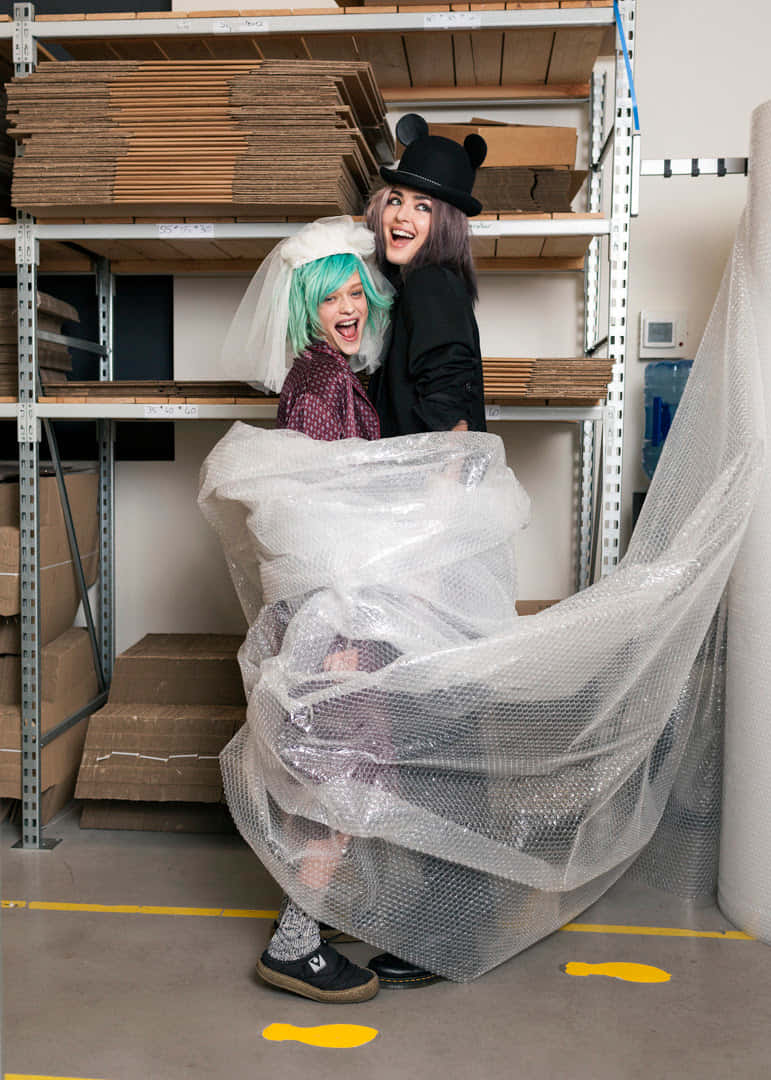 Clothes 桌布 壁紙 — 兩個穿著戲服的快樂人物在充滿紙板架的倉庫中，從泡泡紙後面偷看。