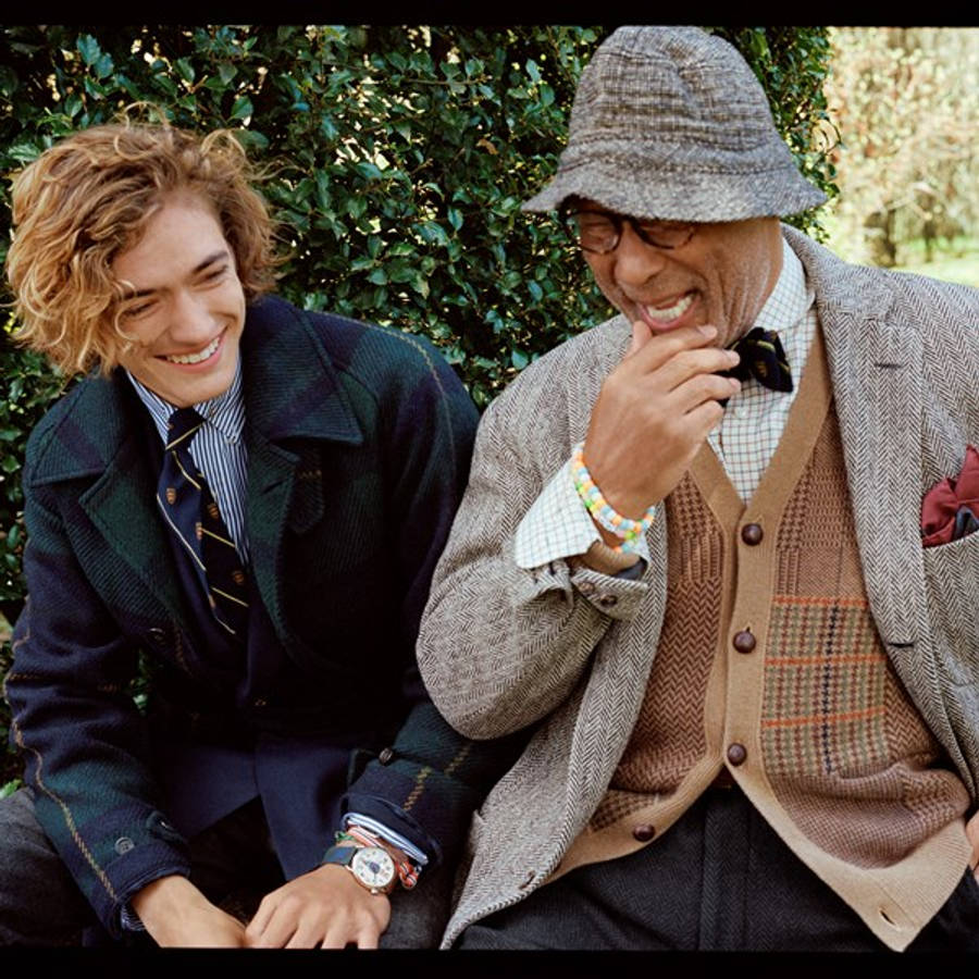 ralph lauren 桌布 壁紙 — 兩個穿著時尚層次服裝的男人在茂密的綠色樹籬背景下分享歡樂的笑聲。