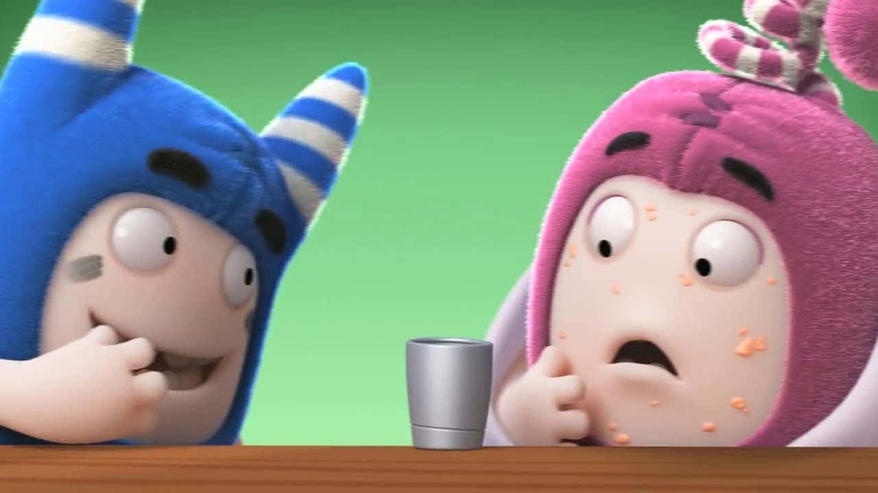 Oddbods 桌布 壁紙 — 兩個穿著毛絨藍色和粉紅色服裝的卡通角色，對木桌上的一個小銀杯表現出驚訝的反應。