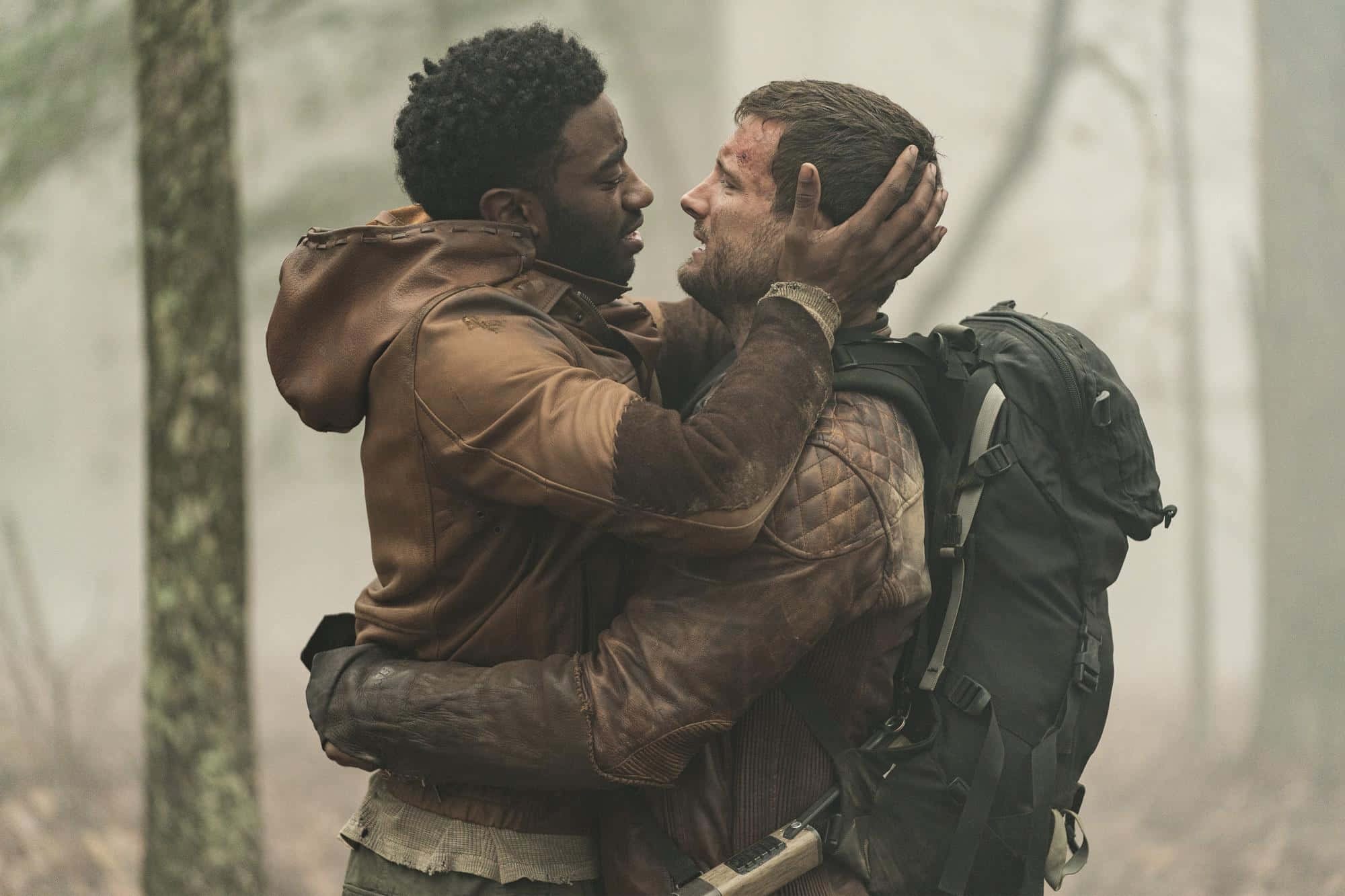 walking dead 桌布 壁紙 — 兩個穿著泥濘皮夾克的男人在霧氣瀰漫的森林中緊緊擁抱，其中一人深情地捧著對方的臉。