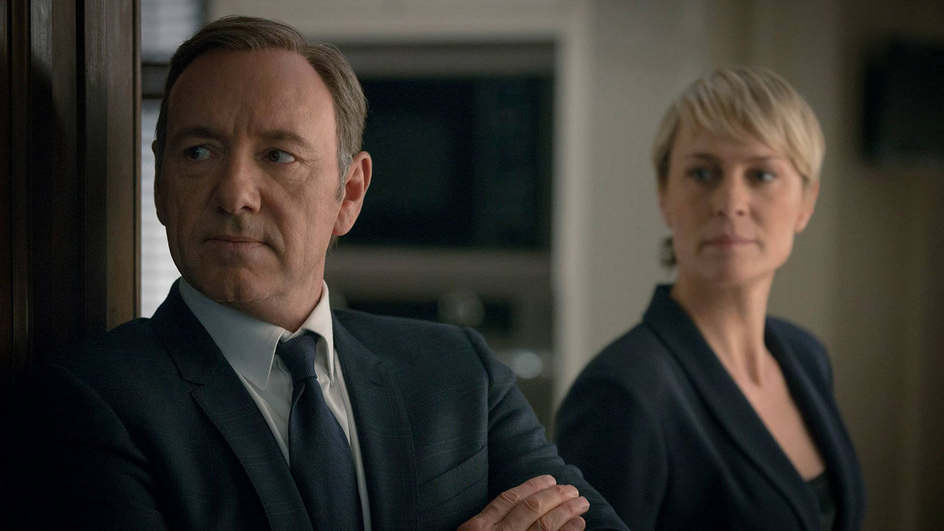 kevin spacey 桌布 壁紙 — 兩個穿著深色西裝的嚴肅人士，在昏暗的房間裡帶著專注的表情站立。