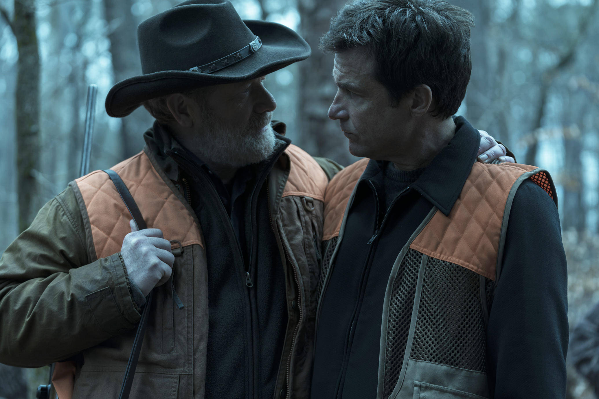 Netflix 桌布 壁紙 — 兩個穿著狩獵背心的男人在霧氣瀰漫的森林中緊密站立，其中一人持步槍，分享著緊張的時刻。