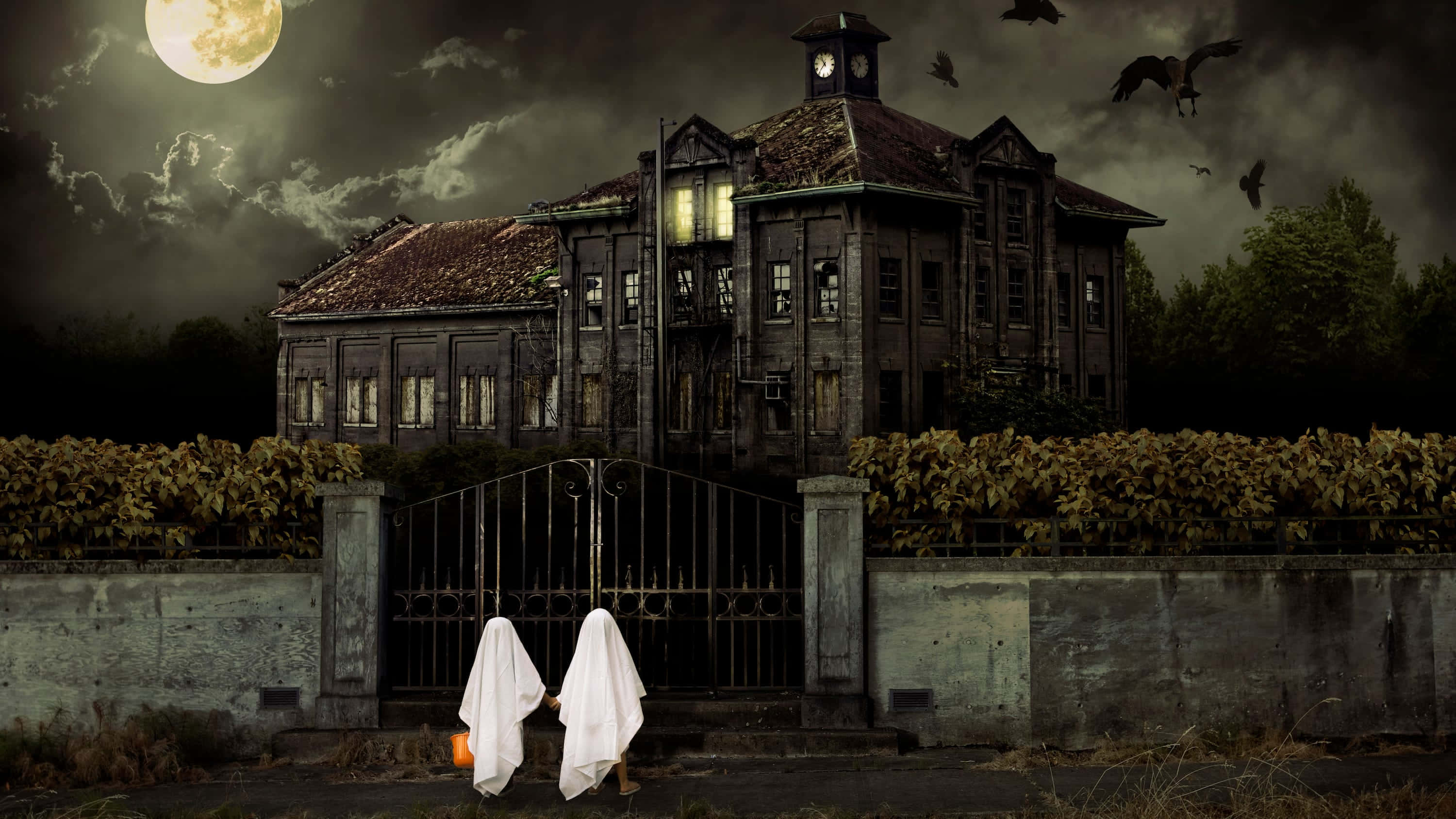 Haunted House 桌布 壁紙 — 兩個穿著白床單的幽靈小孩拿著南瓜，站在滿月下破舊的鬼屋前，烏鴉在頭頂飛過。