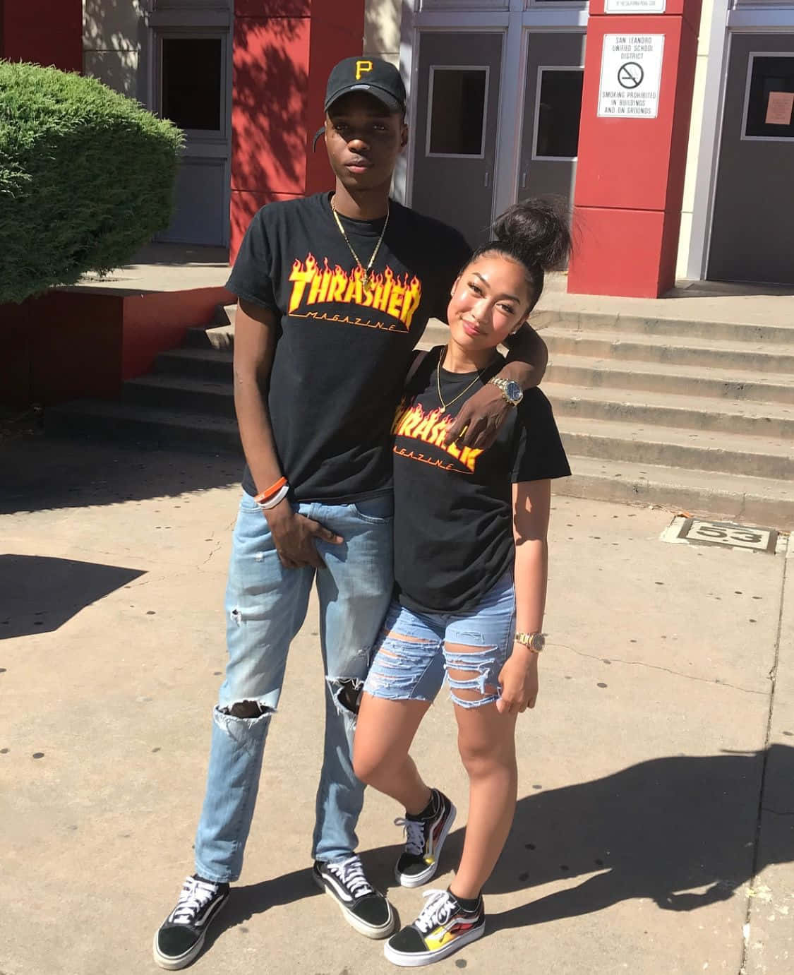 Thrasher 桌布 壁紙 — 兩個穿著相配Thrasher T恤和破洞牛仔褲的青少年在陽光明媚的日子裡自信地在紅色建築物外擺姿勢。