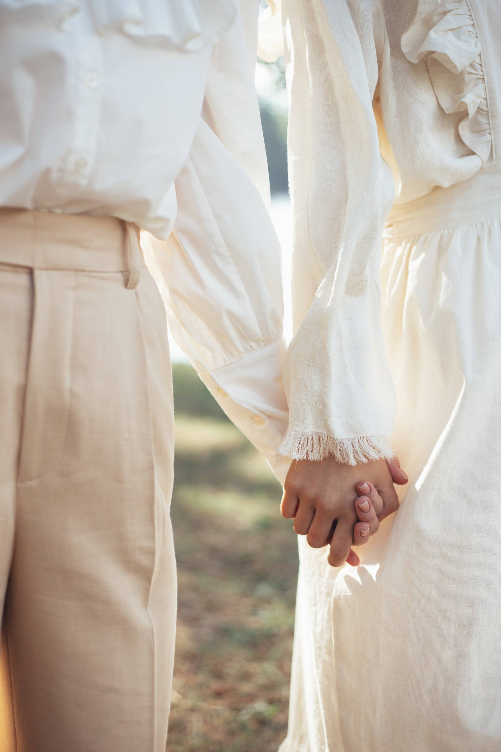 Love And Friendship 桌布 壁紙 — 兩個穿著米色衣服的人在柔和自然光線下牽手，背景是模糊的戶外景色。