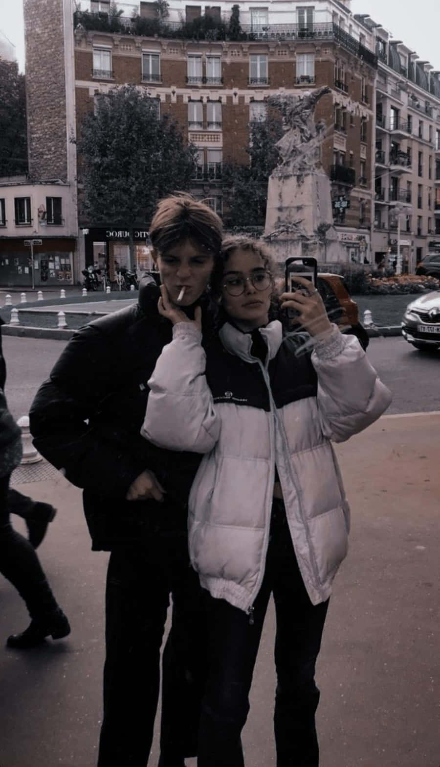 Boyfriend And Girlfriend 桌布 壁紙 — 兩個穿著羽絨外套的年輕人在一個歐洲城市廣場自拍，背景有歷史建築和雕像。