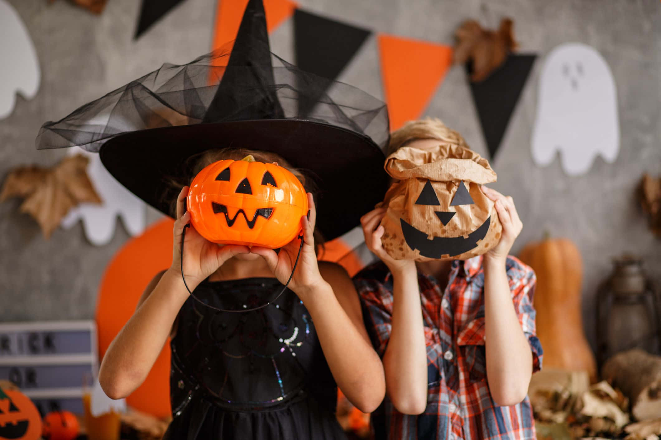 Halloween Pumpkin 桌布 壁紙 — 兩個穿著萬聖節服裝的孩子在裝飾牆前用傑克南瓜燈遮住臉。