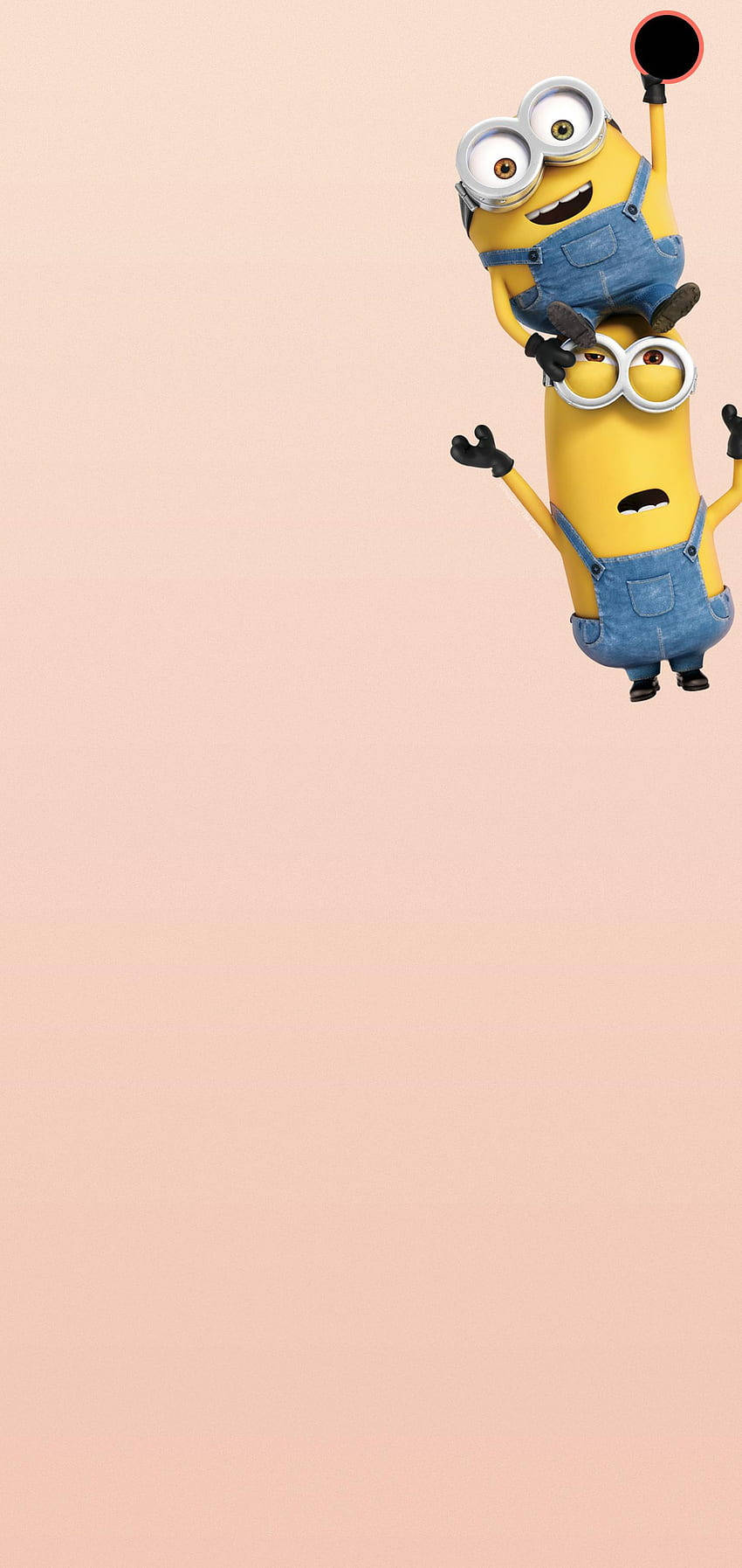 Minion Phone 桌布 壁紙 — 兩個穿著藍色工裝褲的快樂黃色Minions在柔和的粉紅色背景前頑皮地疊在一起，其中一個拿著一個黑色圓形物體。