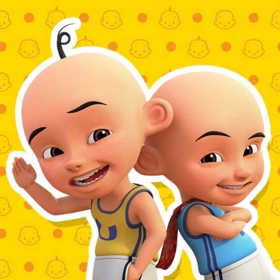 Upin Ipin 桌布 壁紙 — 兩個穿著運動球衣的開心卡通嬰兒，在帶有重複嬰兒臉部圖案的亮黃色背景上揮手微笑。