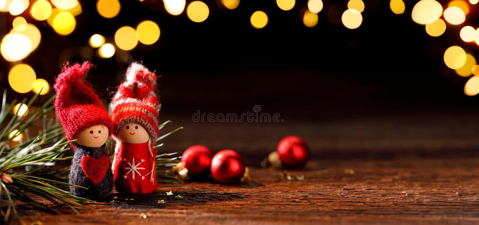 Funny Holiday Desktop 桌布 壁紙 — 兩個節日編織人物戴著紅帽，站在松針和裝飾品旁邊，背景是溫暖的散景燈光。