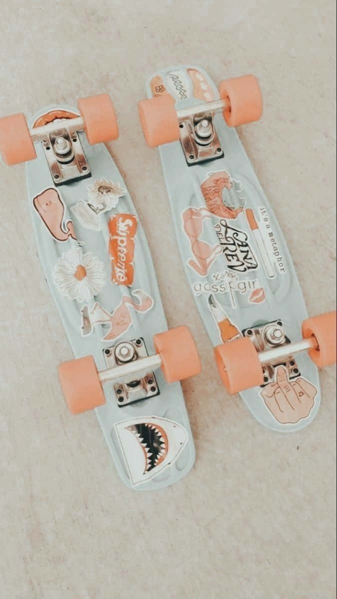 Peachy Aesthetic 桌布 壁紙 — 兩個粉彩色滑板，配有蜜桃色輪子和可愛貼紙，並排放在淺色瓷磚地板上。