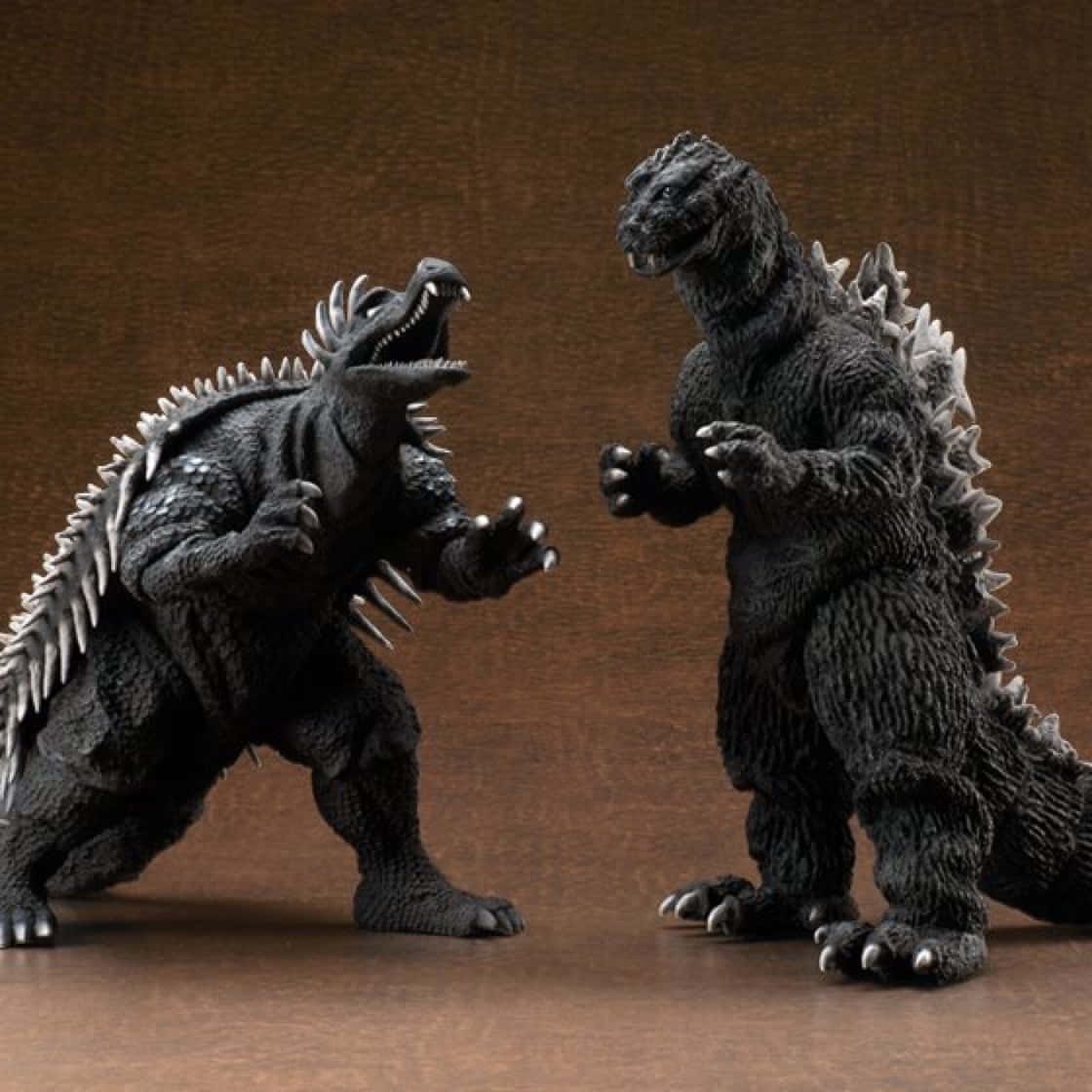 Godzilla Vs Anguirus 桌布 壁紙 — 兩個精細的哥吉拉動作人偶在純棕色背景前進行戲劇性的對峙。