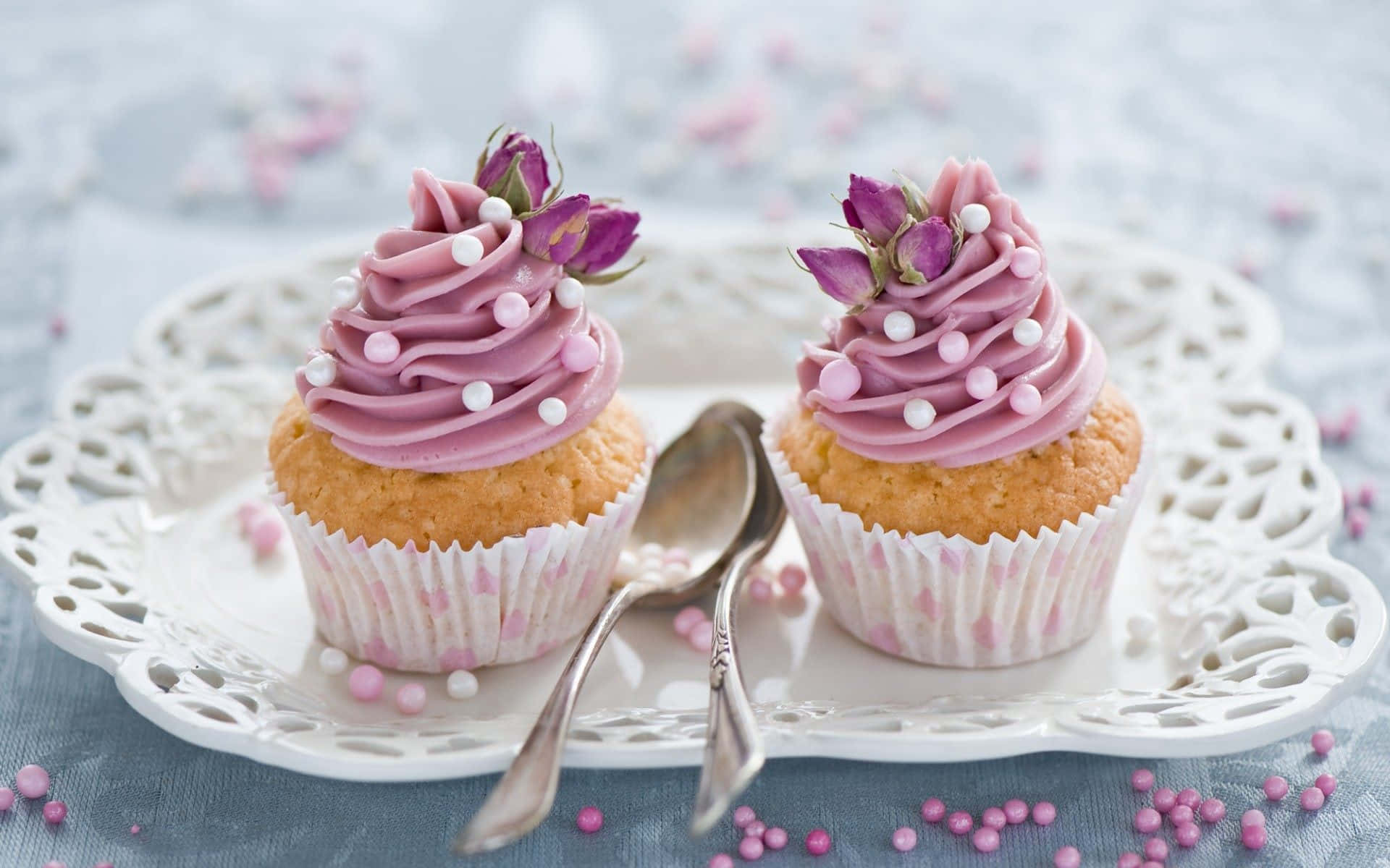 Cute Cupcake 桌布 壁紙 — 兩個精緻的杯子蛋糕，帶有粉紅色糖霜和乾花，放在一個裝飾性的白色盤子上，撒有糖粒。